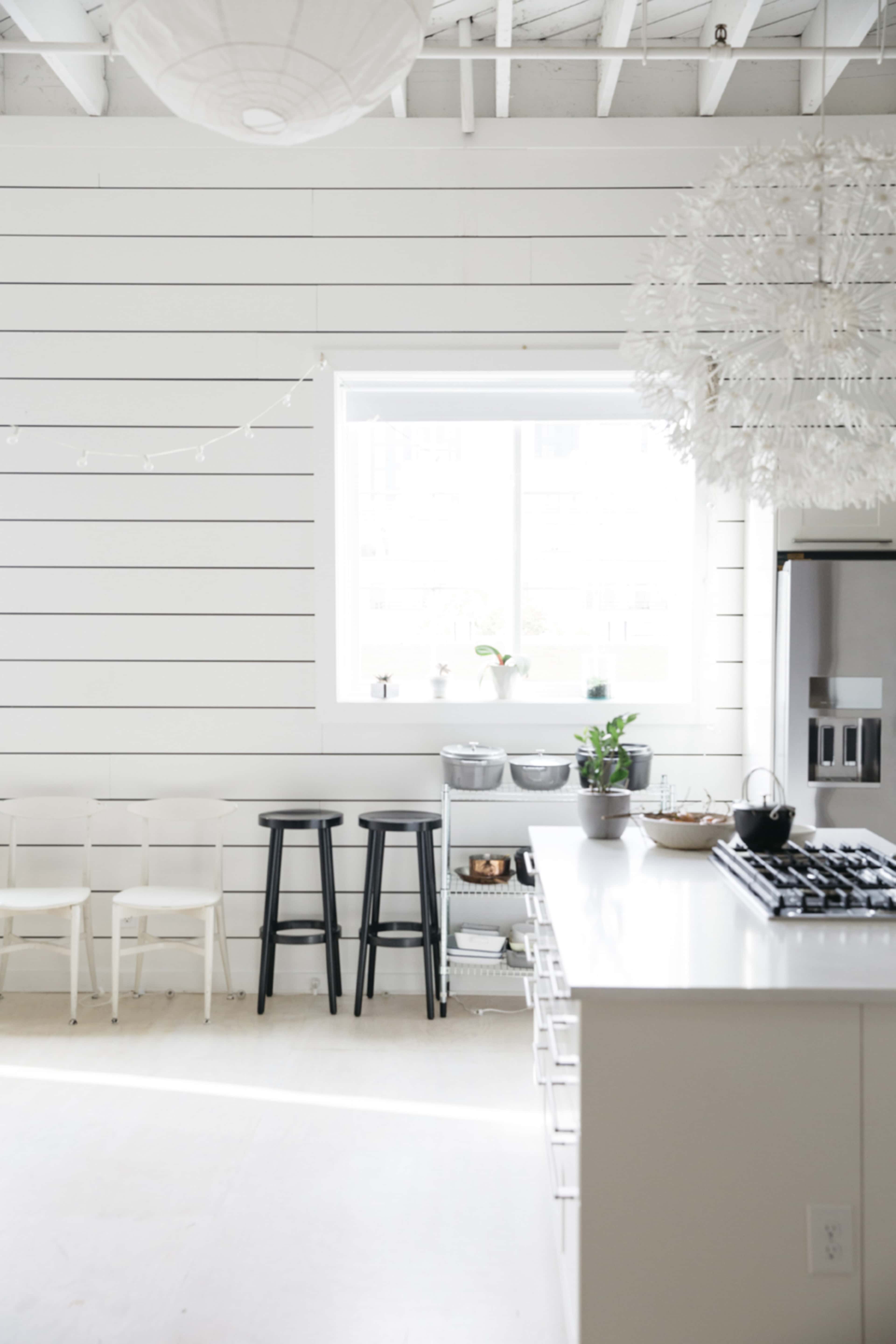 A bright kitchen features a large window, white shiplap walls, contemporary bar stools, and a modern gas stove with an island.