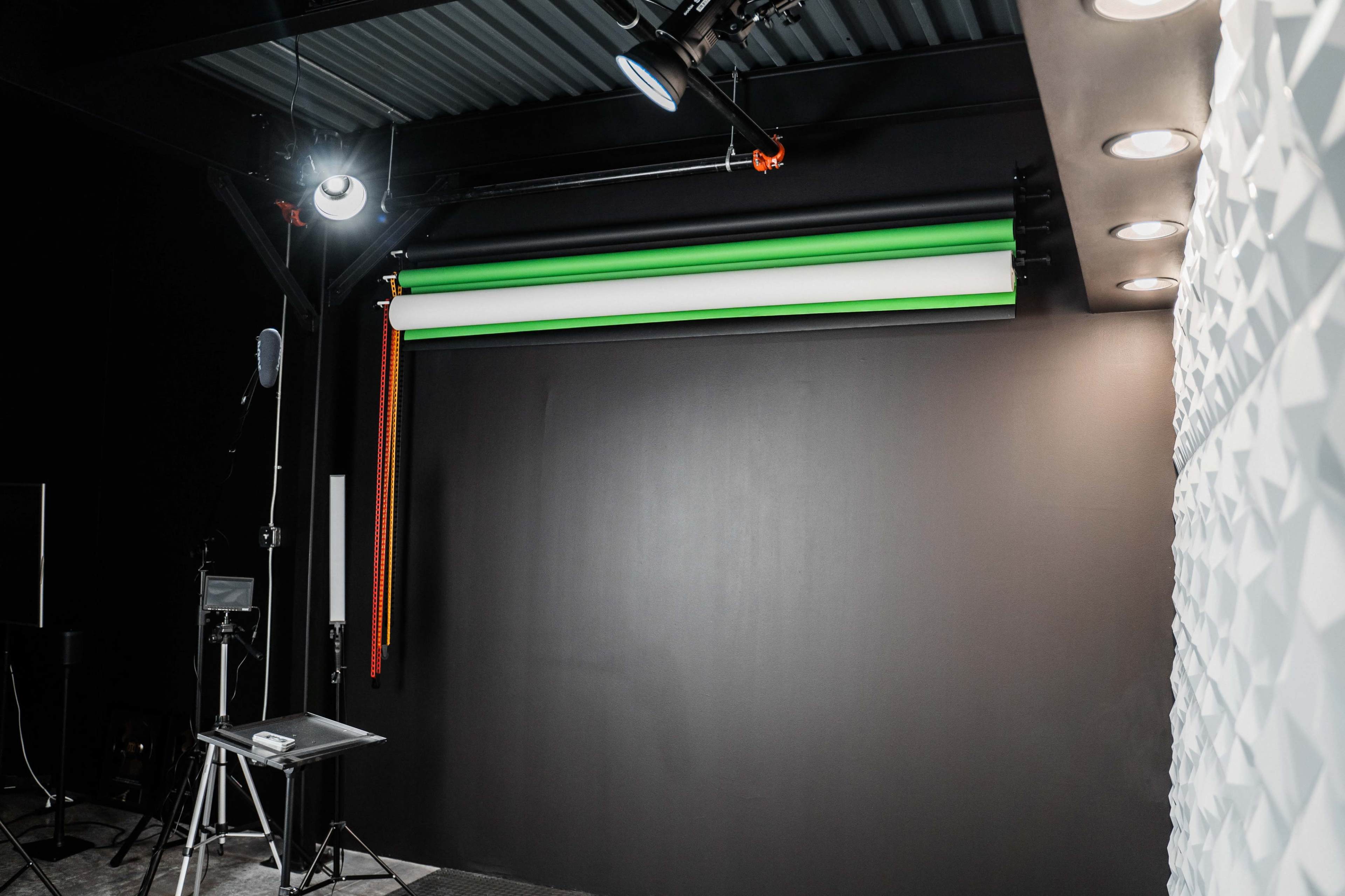 A photography studio features a dark background with green and white seamless backdrop rolls, studio lighting, and equipment positioned around the space.