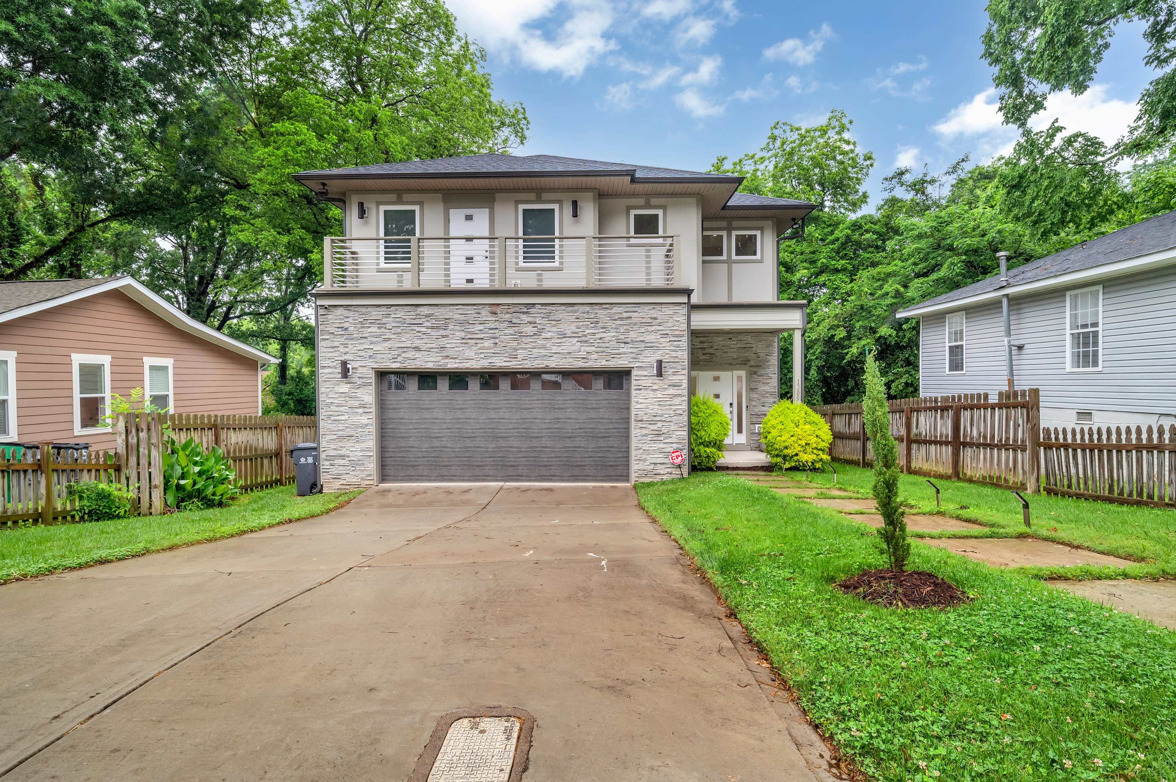 A two-story house with a stone front facade and a garage is set on a landscaped lawn with a paved driveway and neighboring homes.