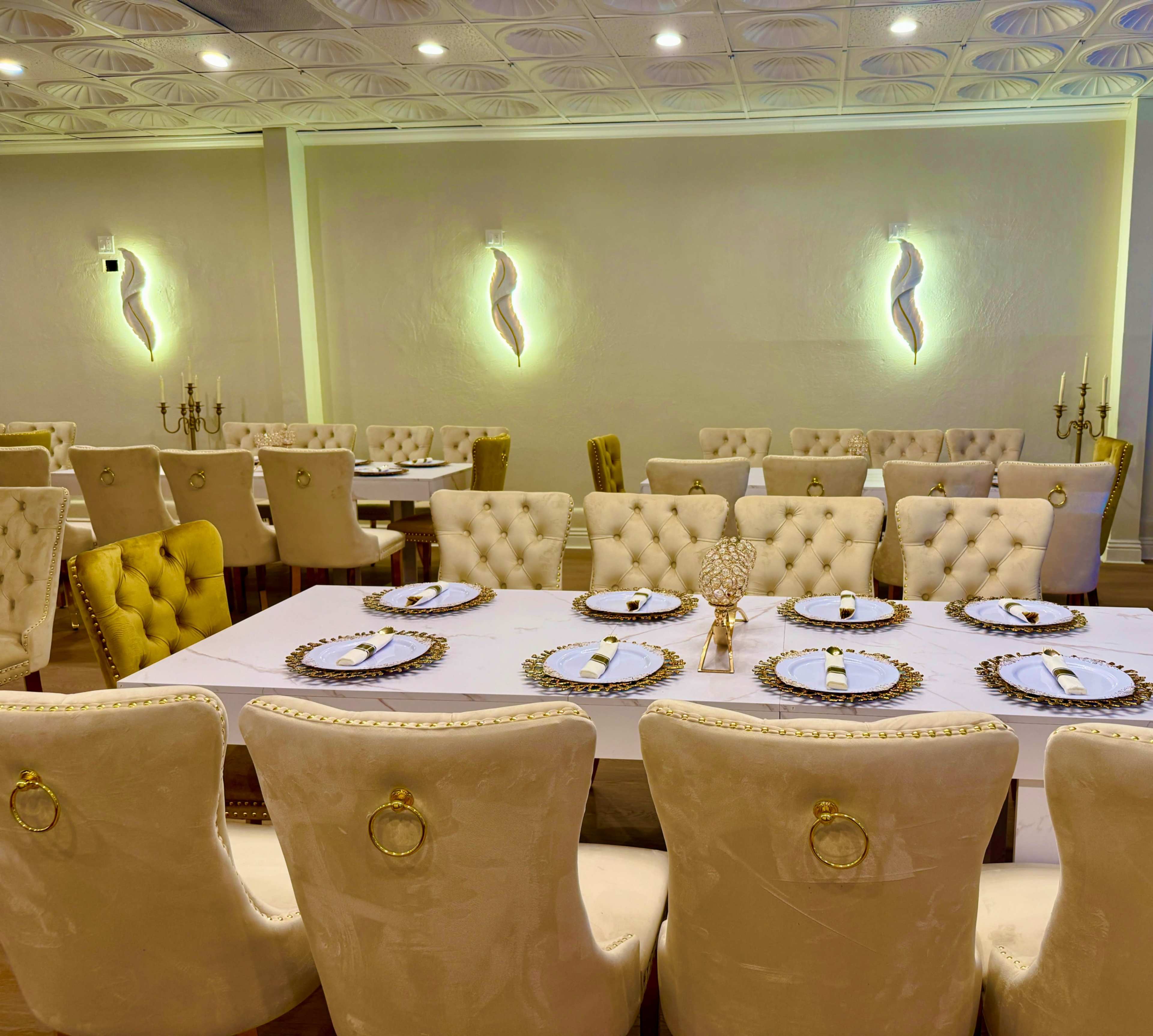 The image shows an elegantly arranged dining area with plush, cream-colored chairs and a long table set with decorative plates and napkins.