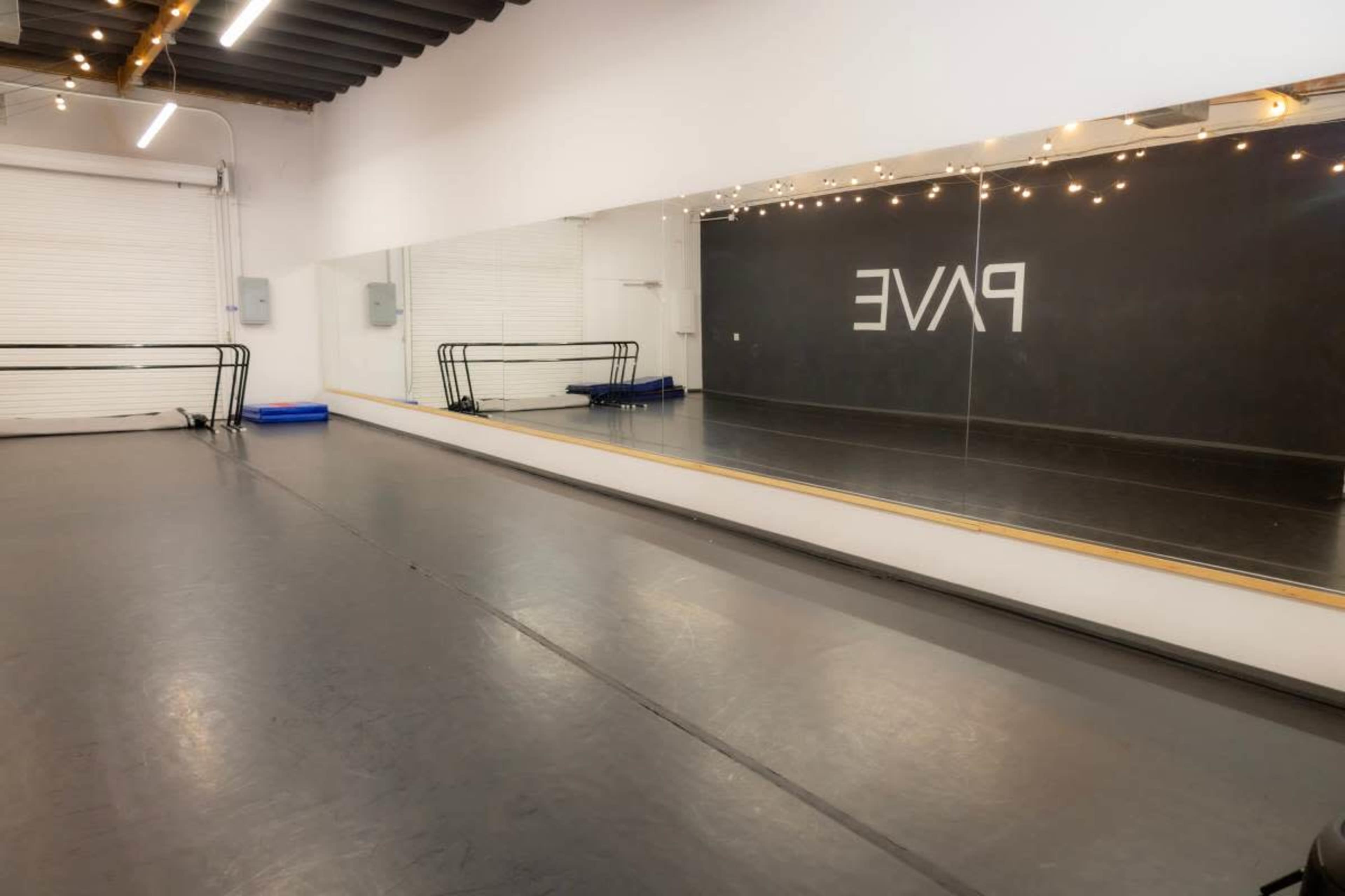 The image shows a dance studio with a reflective mirror wall, ballet bars, and a clean, polished floor.