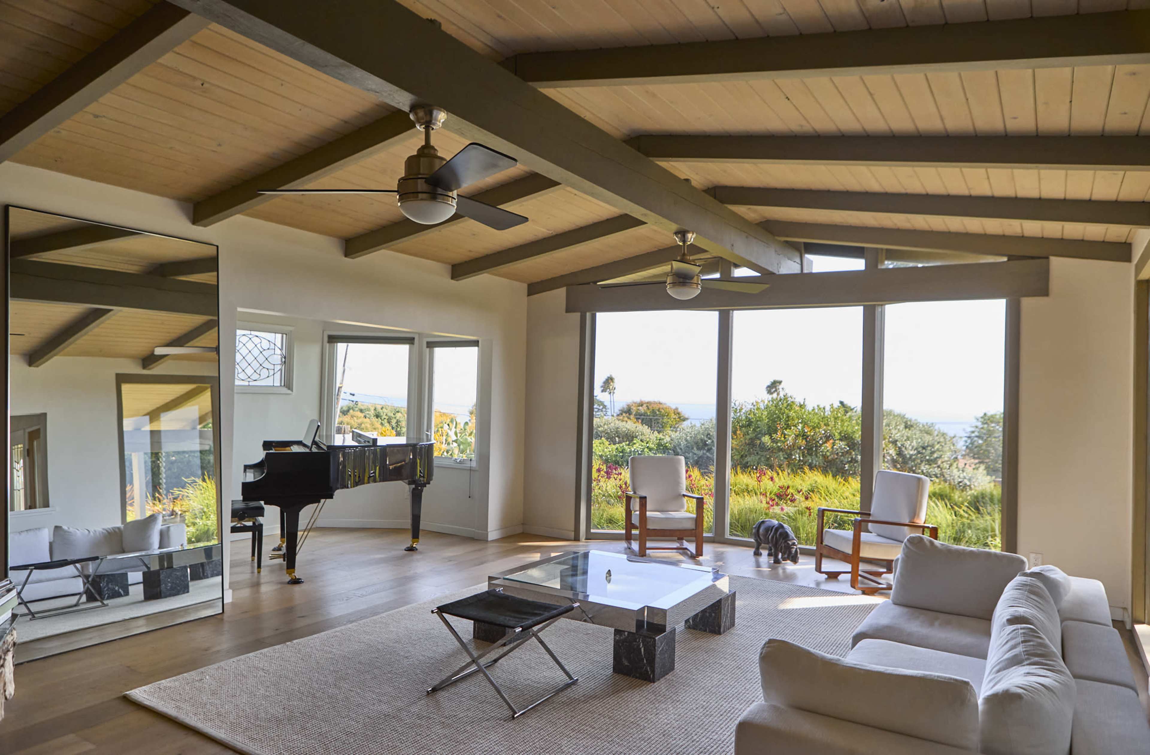 The living room features large windows, a piano, a minimalist couch, and a coffee table, with a view of the outdoors.