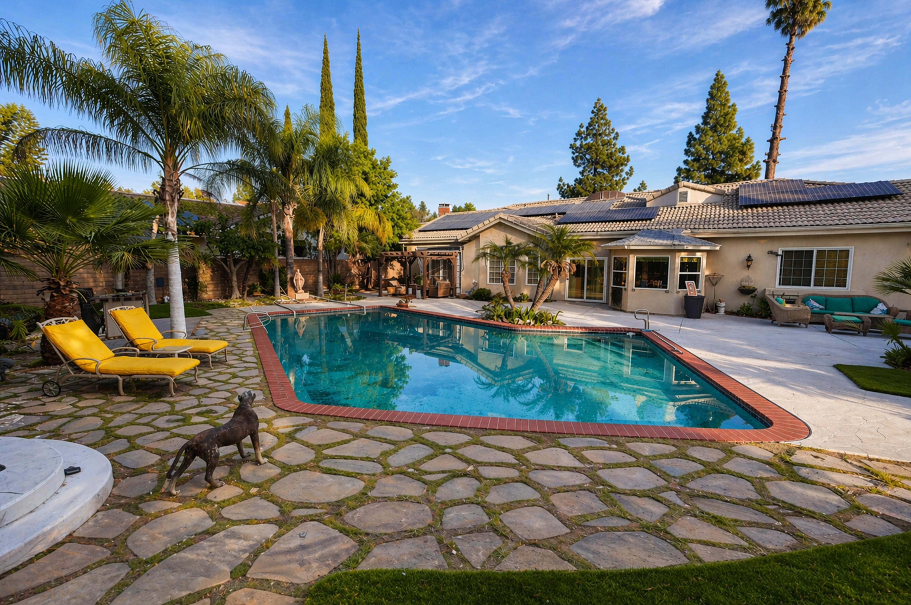 The scene shows a residential backyard with a swimming pool surrounded by palm trees, stone pathways, and lounge chairs.