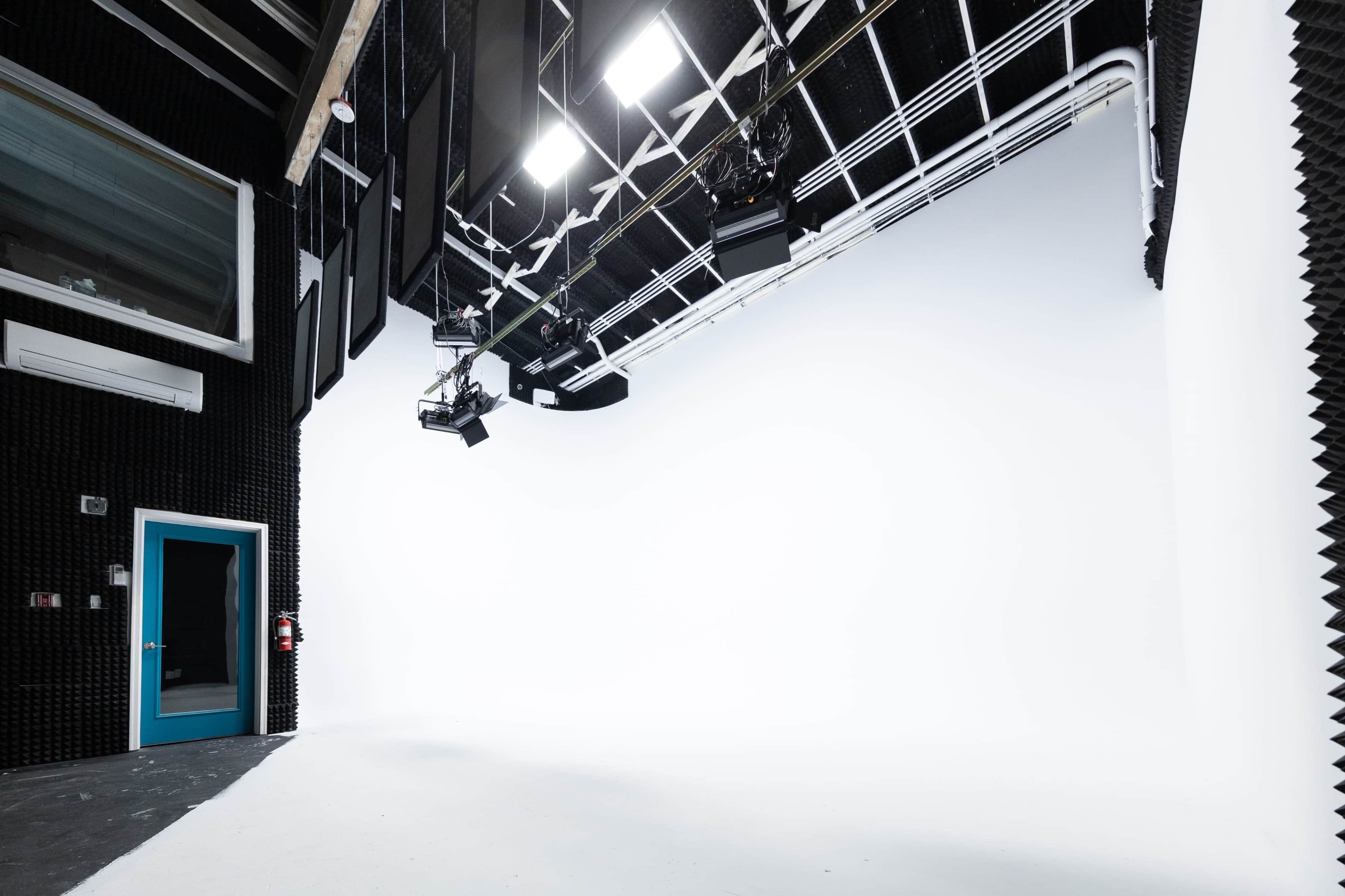A spacious, empty studio with a white backdrop, studio lights, and soundproofing panels on the walls.