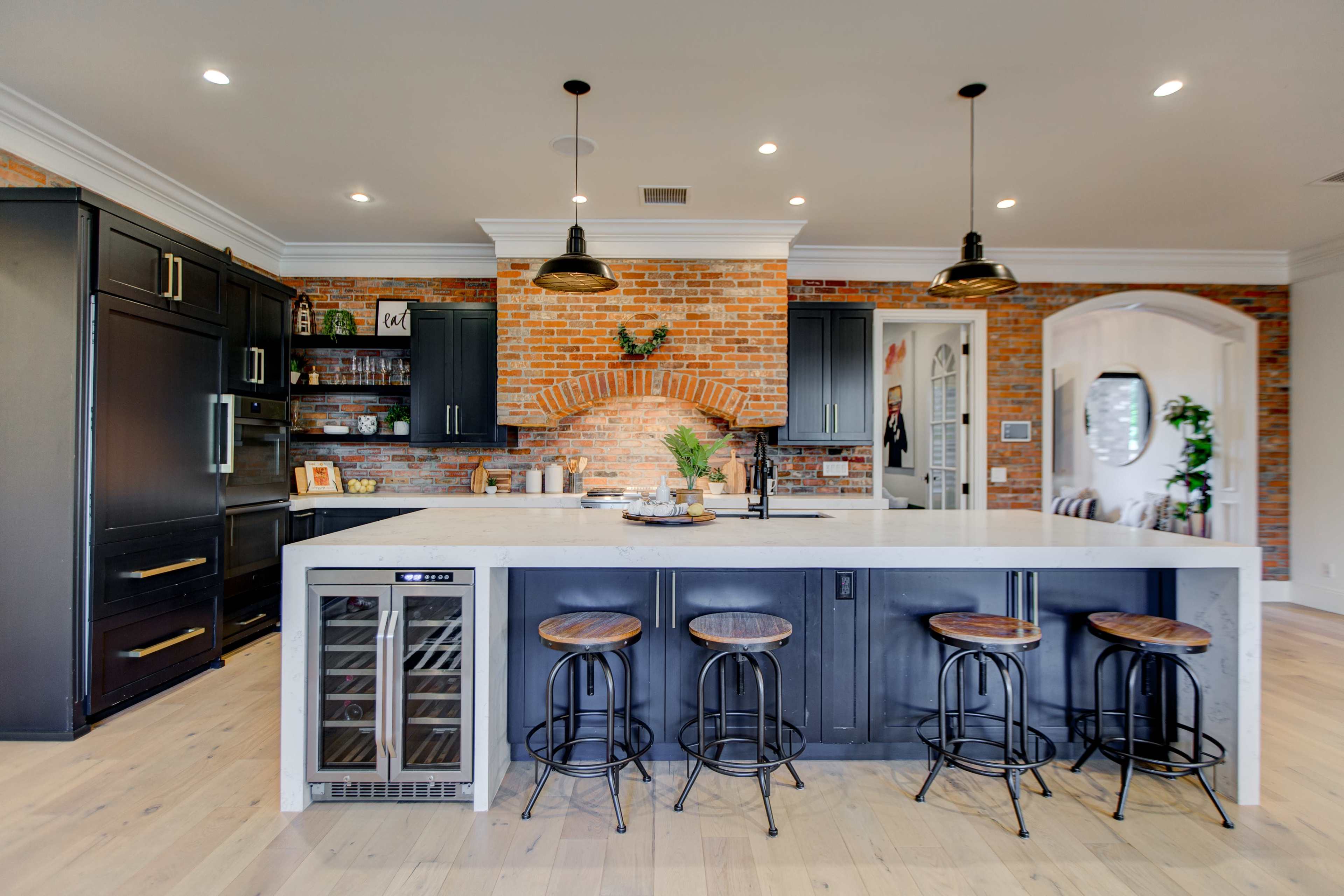 The kitchen features a large island with seating, black cabinetry, a brick arch, and modern lighting fixtures.