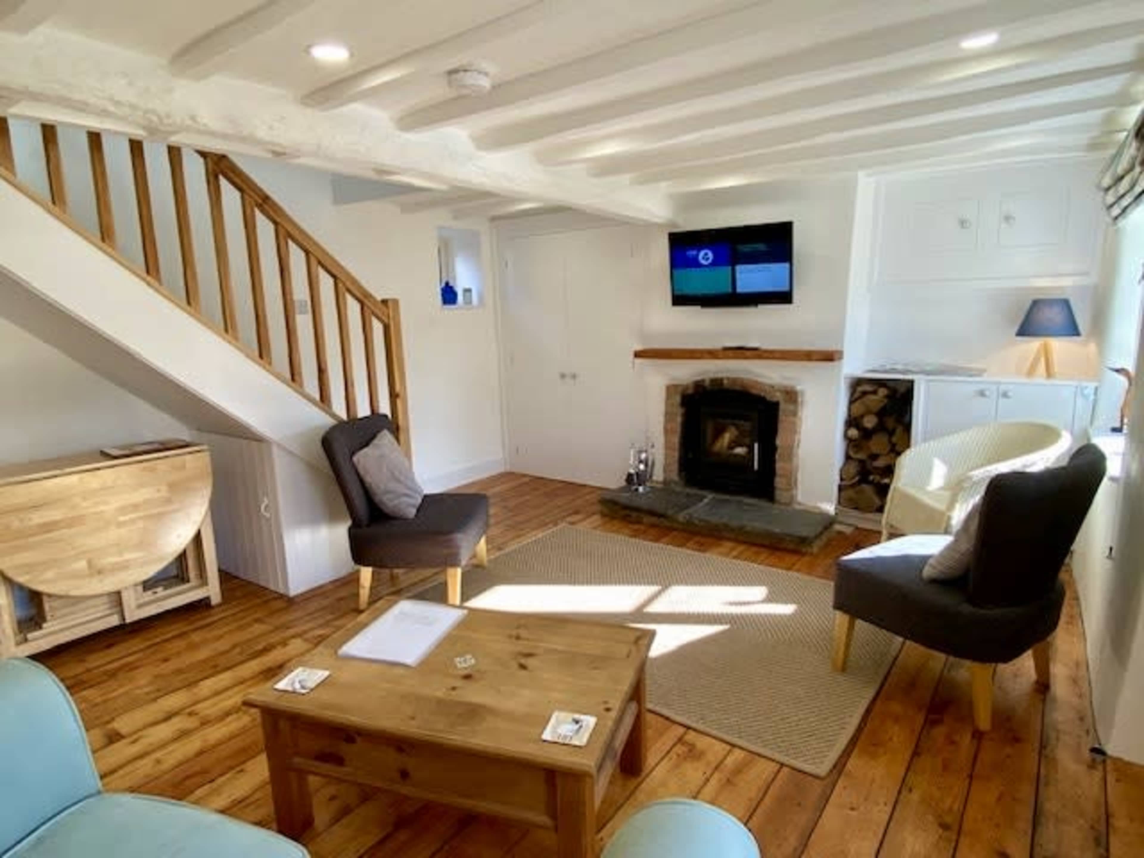 The room features a cozy living area with a wooden floor, a fireplace, a television mounted on the wall, and a staircase leading to the upper level.