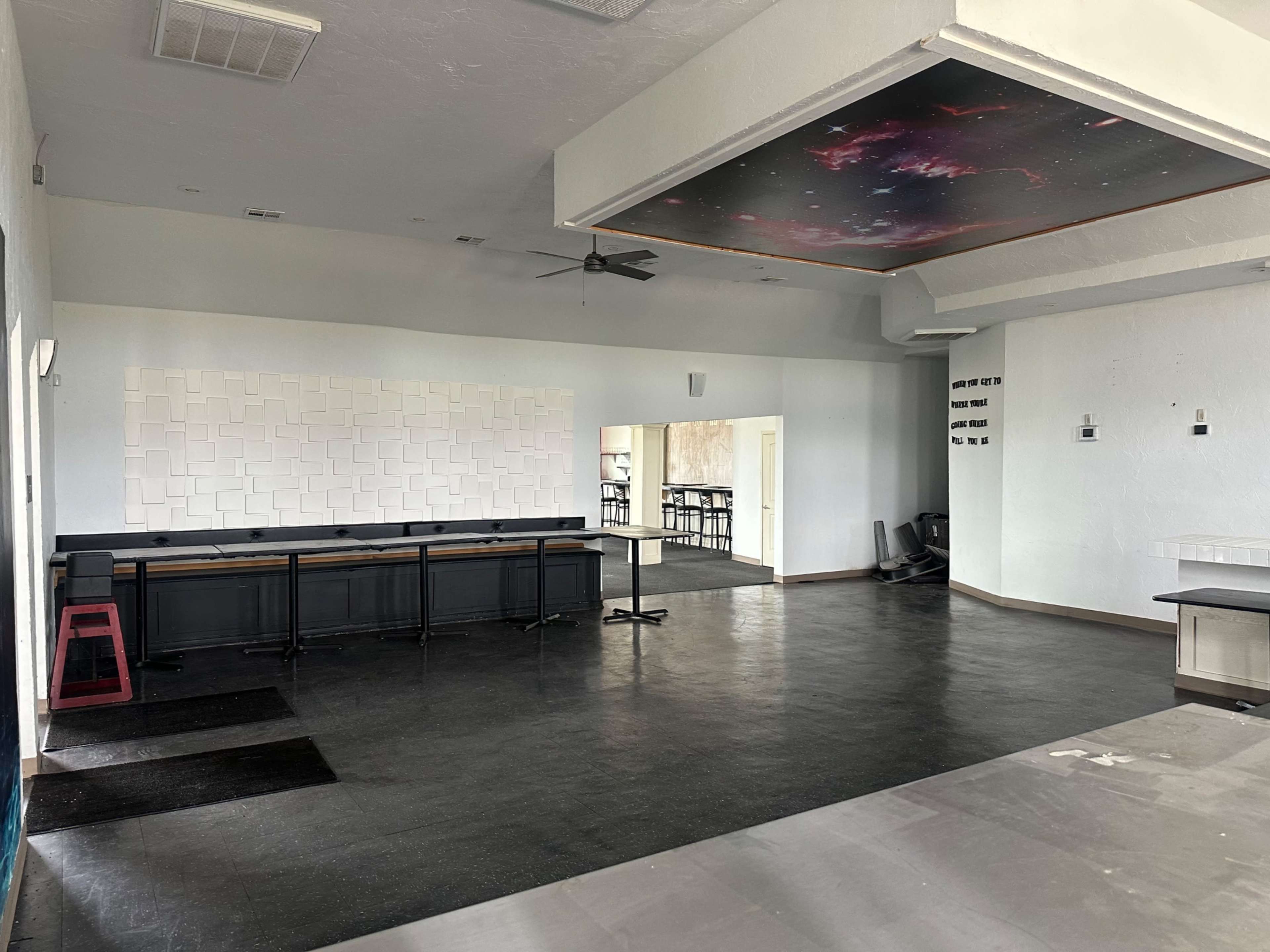 The image shows an empty room with a bar area, a patterned wall, and an entrance leading to another space.
