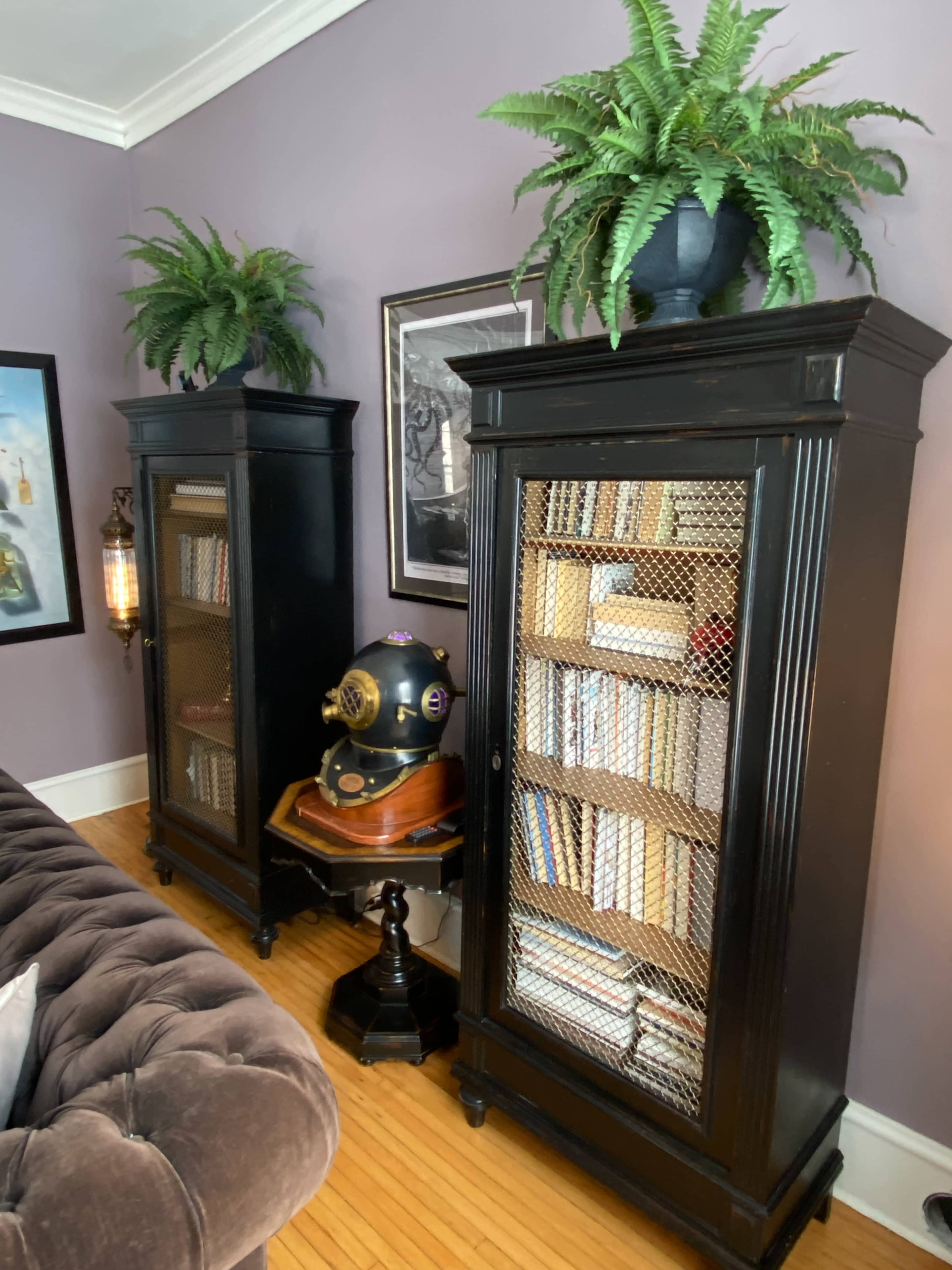 The image shows two black wooden bookcases with glass doors and a decorative diving helmet on a side table between them, all set against a purple wall.