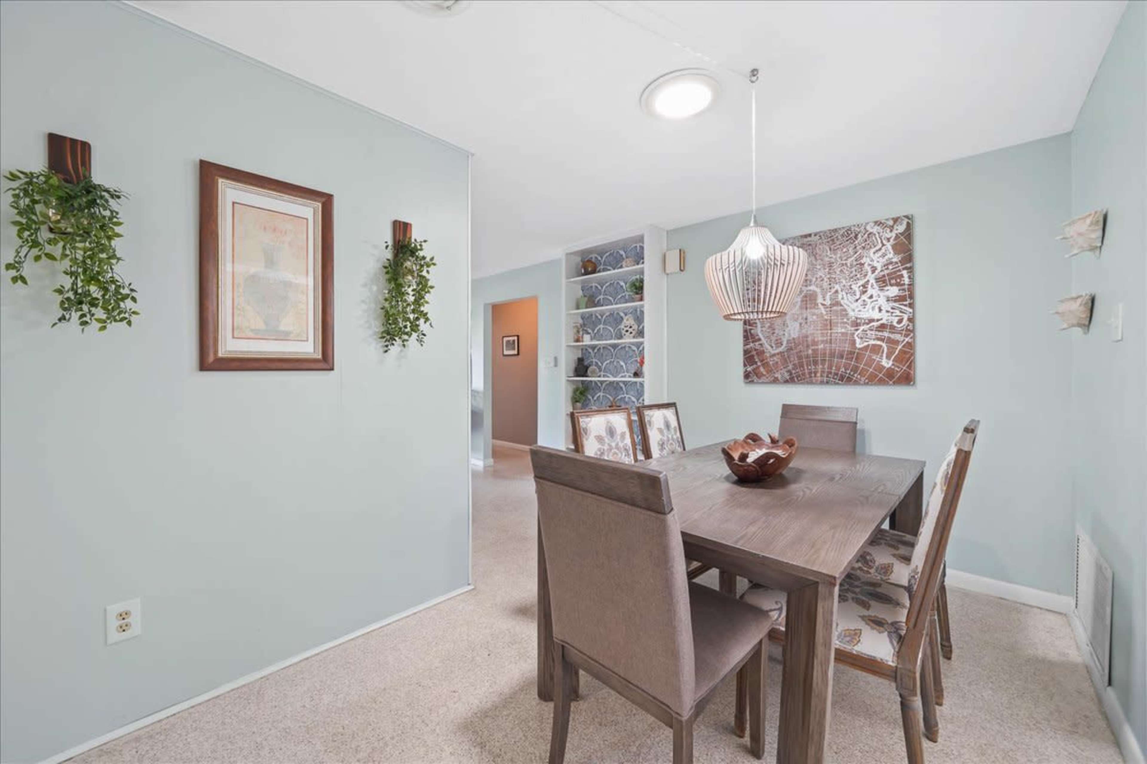 A dining area features a wooden table surrounded by six chairs, with light green walls and decorative wall hangings.
