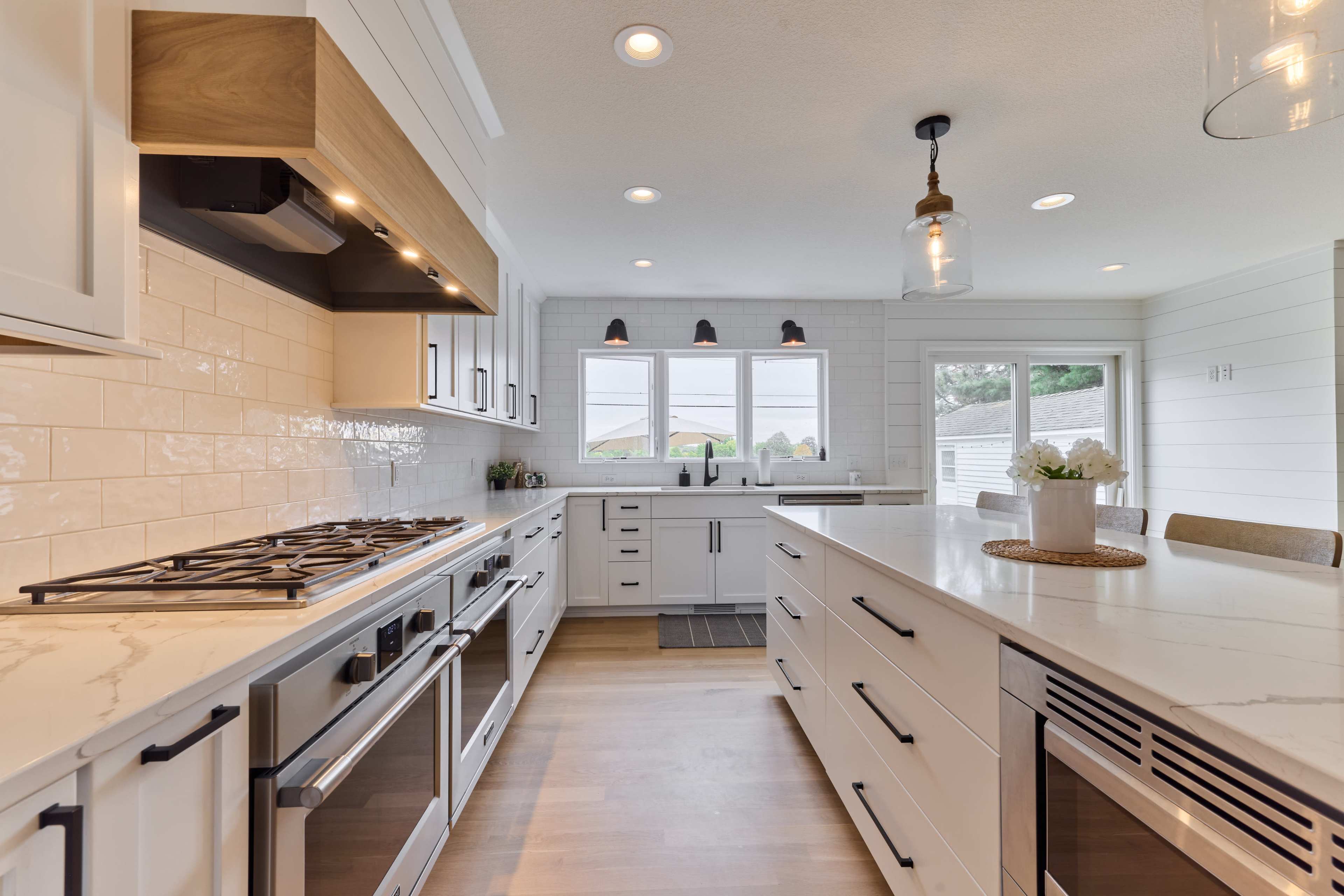 A modern kitchen features white cabinetry, a large island with a marble countertop, and a gas stove with overhead ventilation.