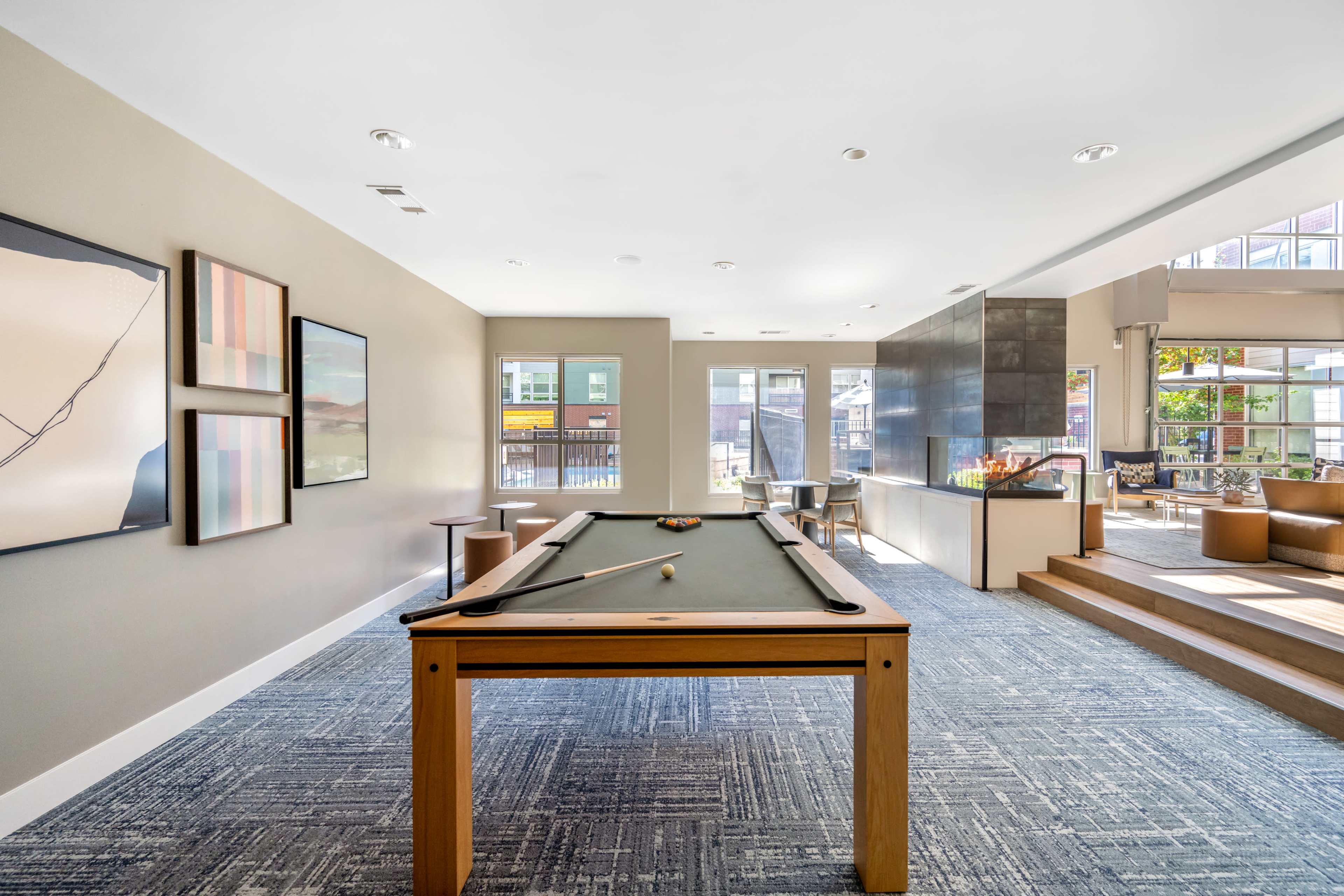 The image shows a spacious lounge area with a pool table, seating arrangements, and large windows allowing natural light.
