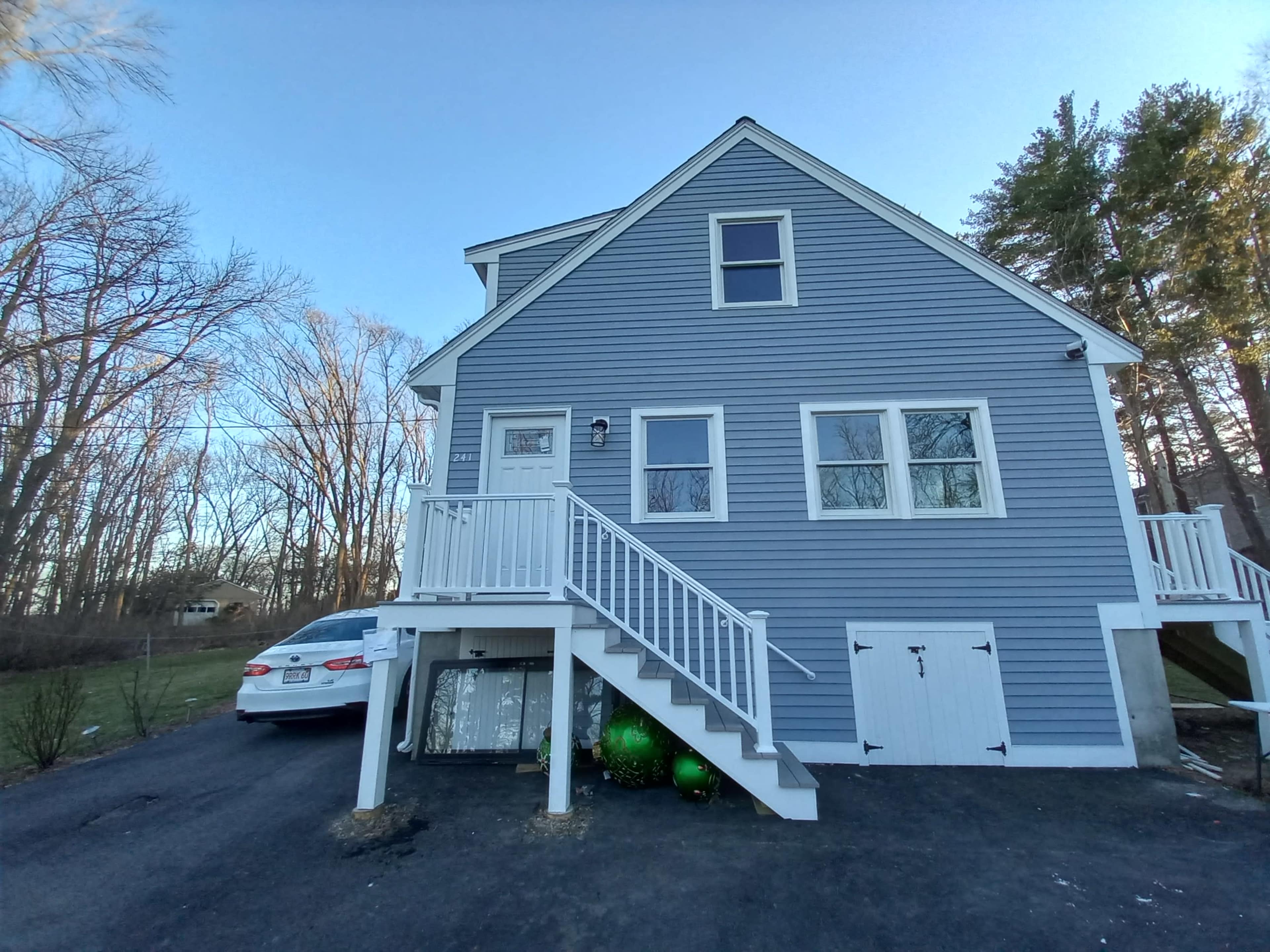 A blue two-story house with white trim and a staircase leading to the front door, accompanied by a parked white car in the driveway.