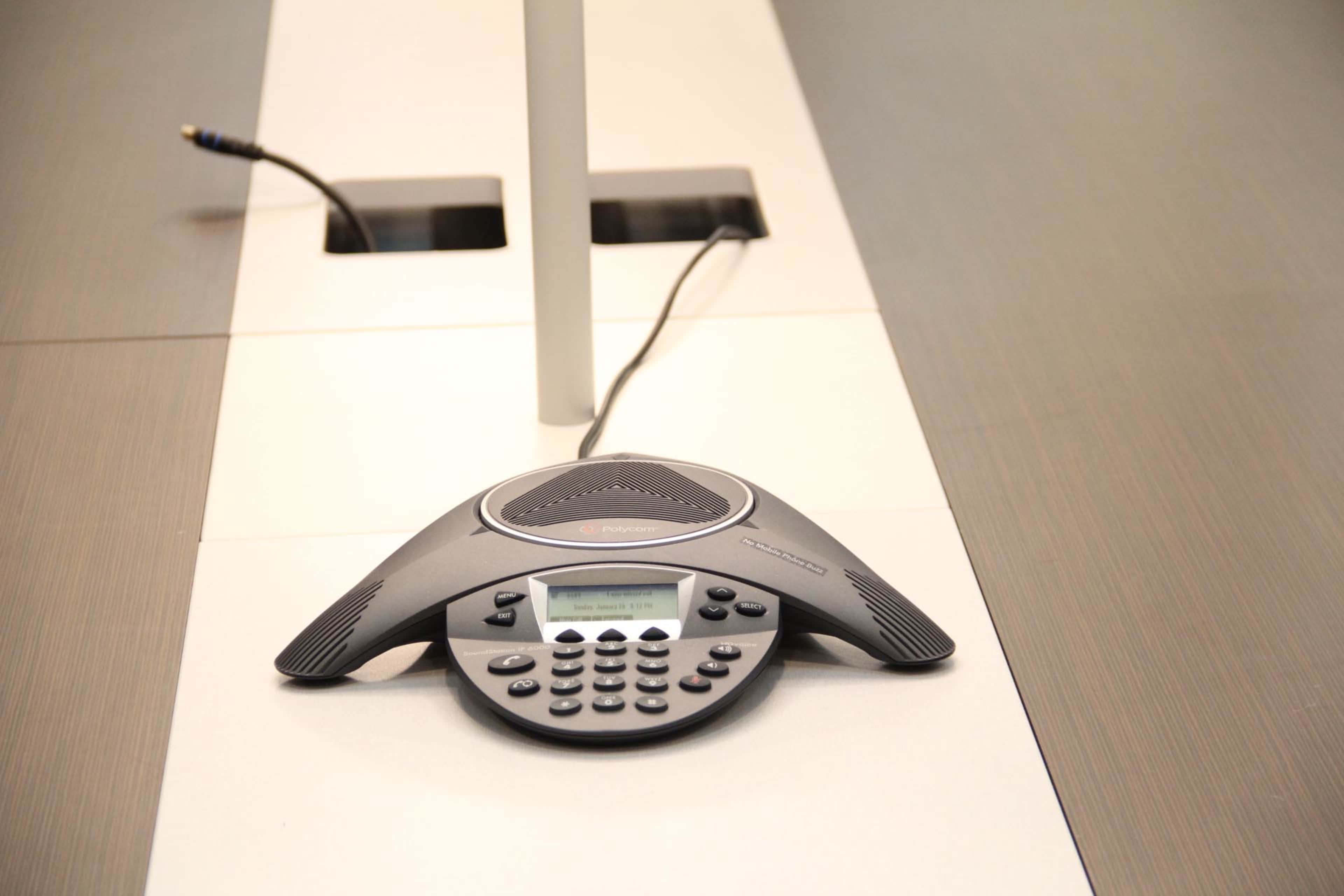 A conference phone with a numeric keypad is positioned on a modern, minimalist table.