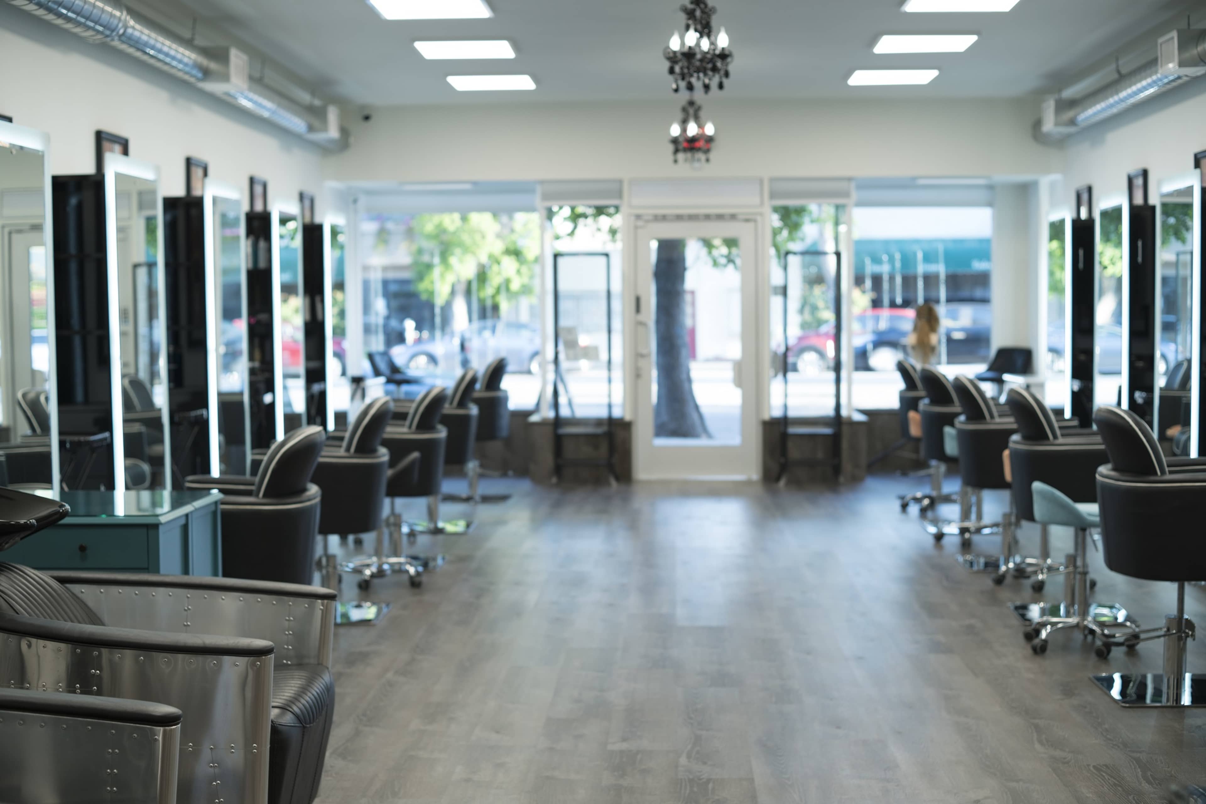 The interior of a modern salon with multiple salon chairs arranged in a row and large mirrors reflecting the space.