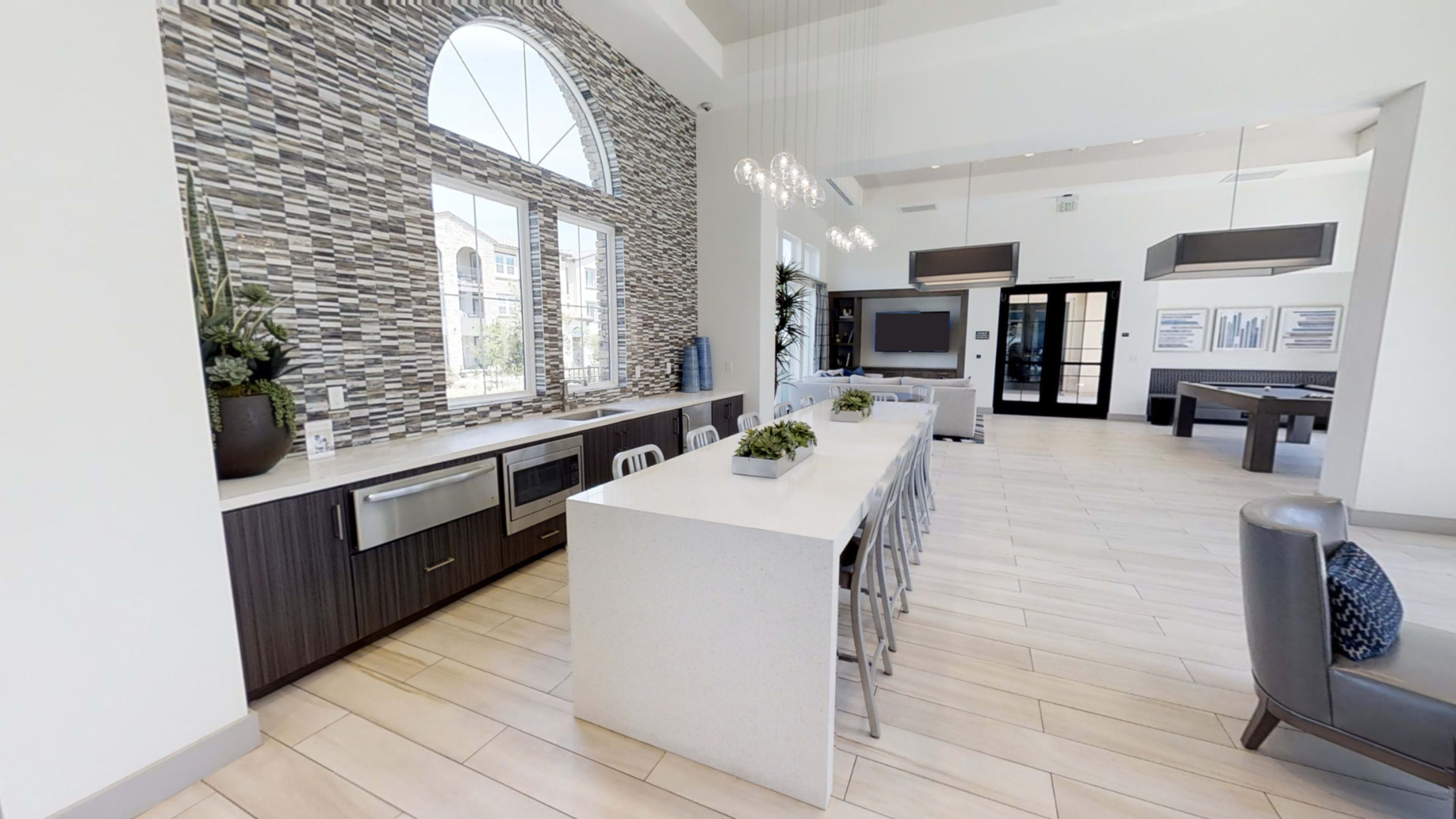 A modern kitchen with a long countertop, stainless steel appliances, and large windows letting in natural light.