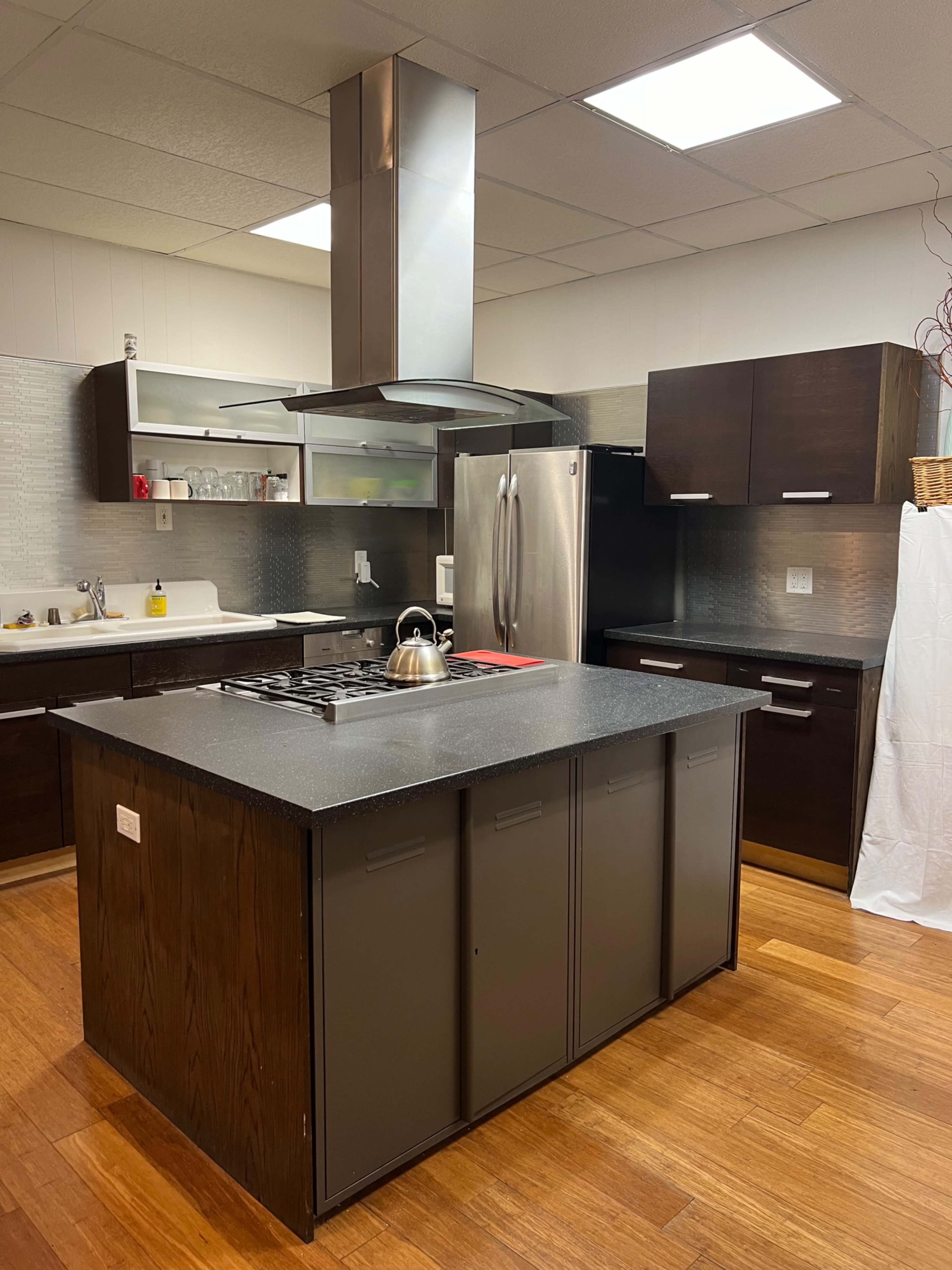 A modern kitchen features dark cabinetry, a central island with a stovetop, and stainless steel appliances.