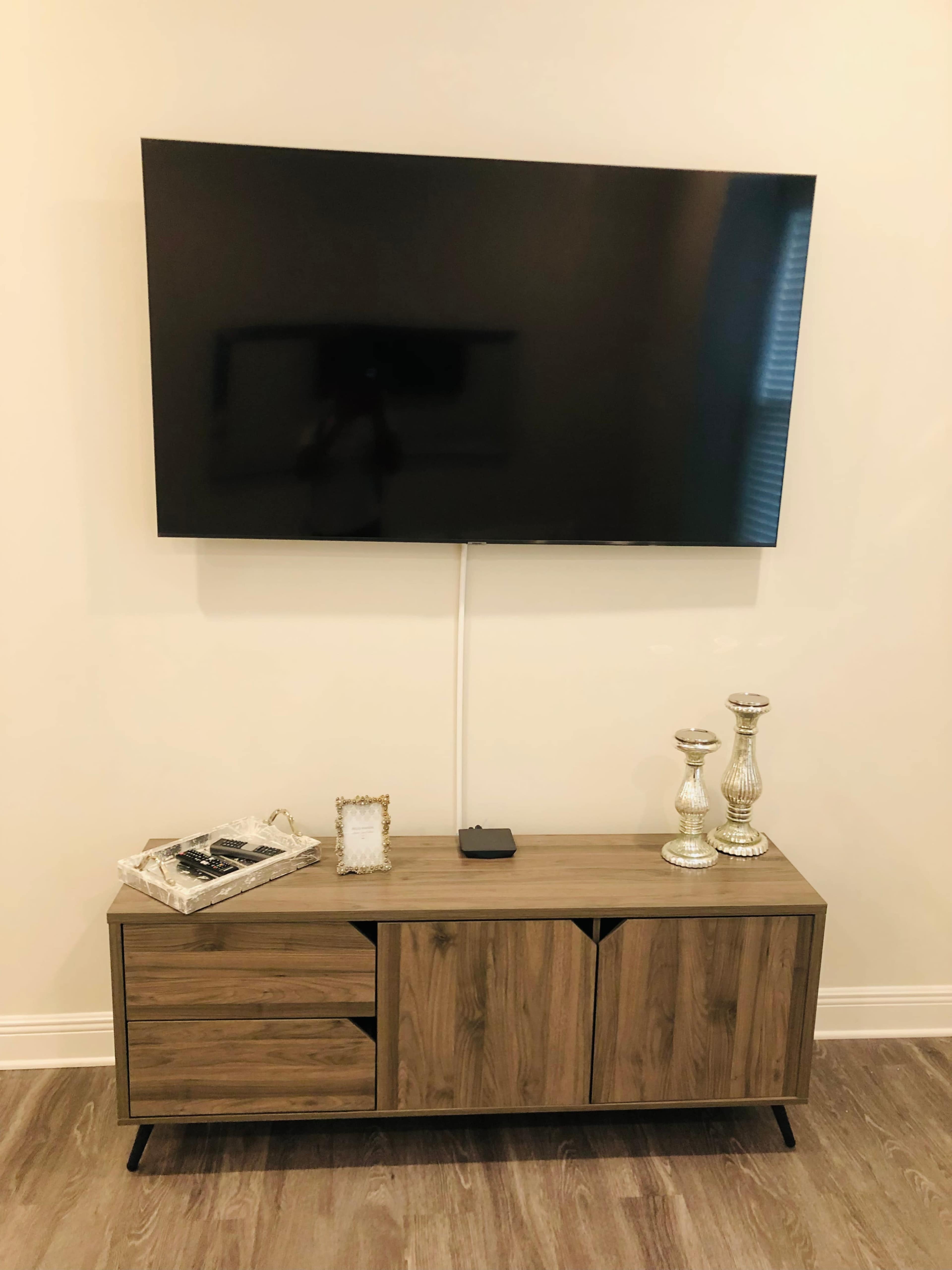 A flat-screen television is mounted on a wall above a wooden TV stand with decorative items and storage compartments.