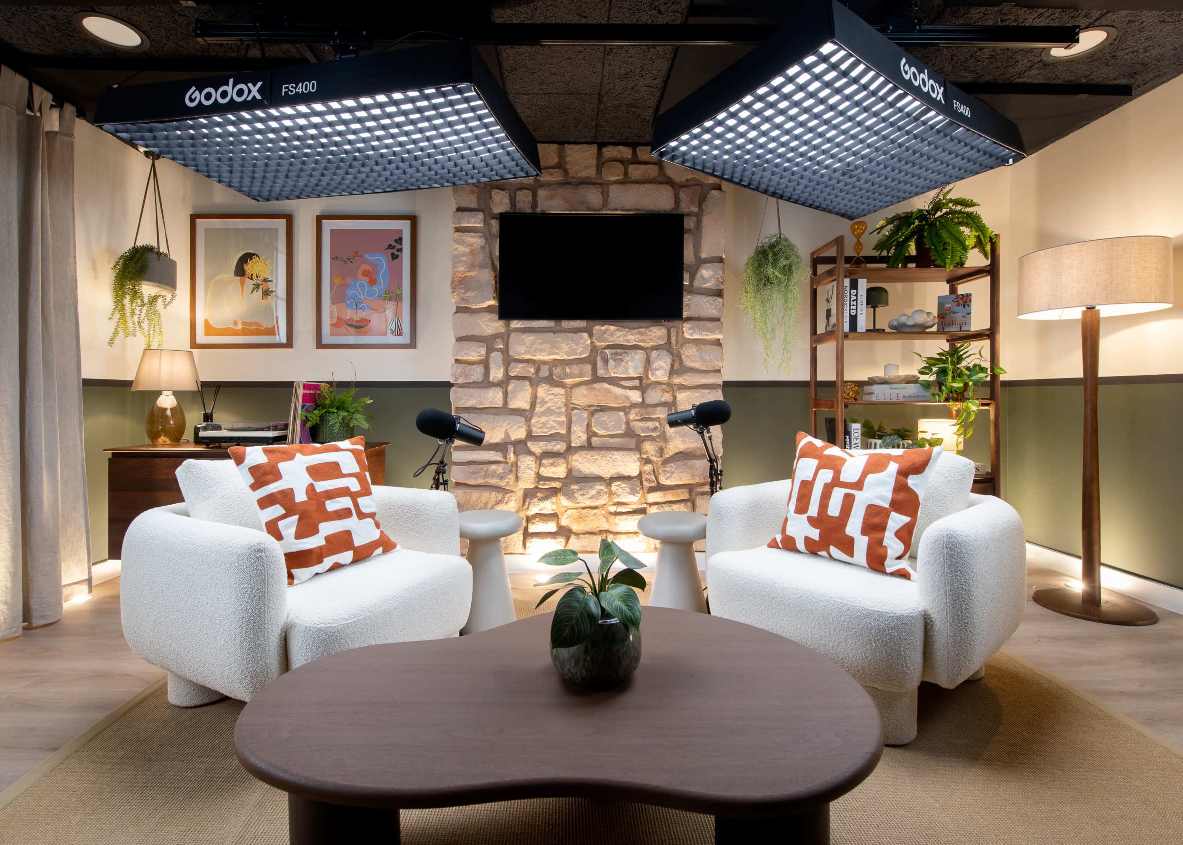 A cozy interior setup featuring two white chairs with orange-patterned cushions, a wooden coffee table, and a stone accent wall, illuminated by overhead lights.