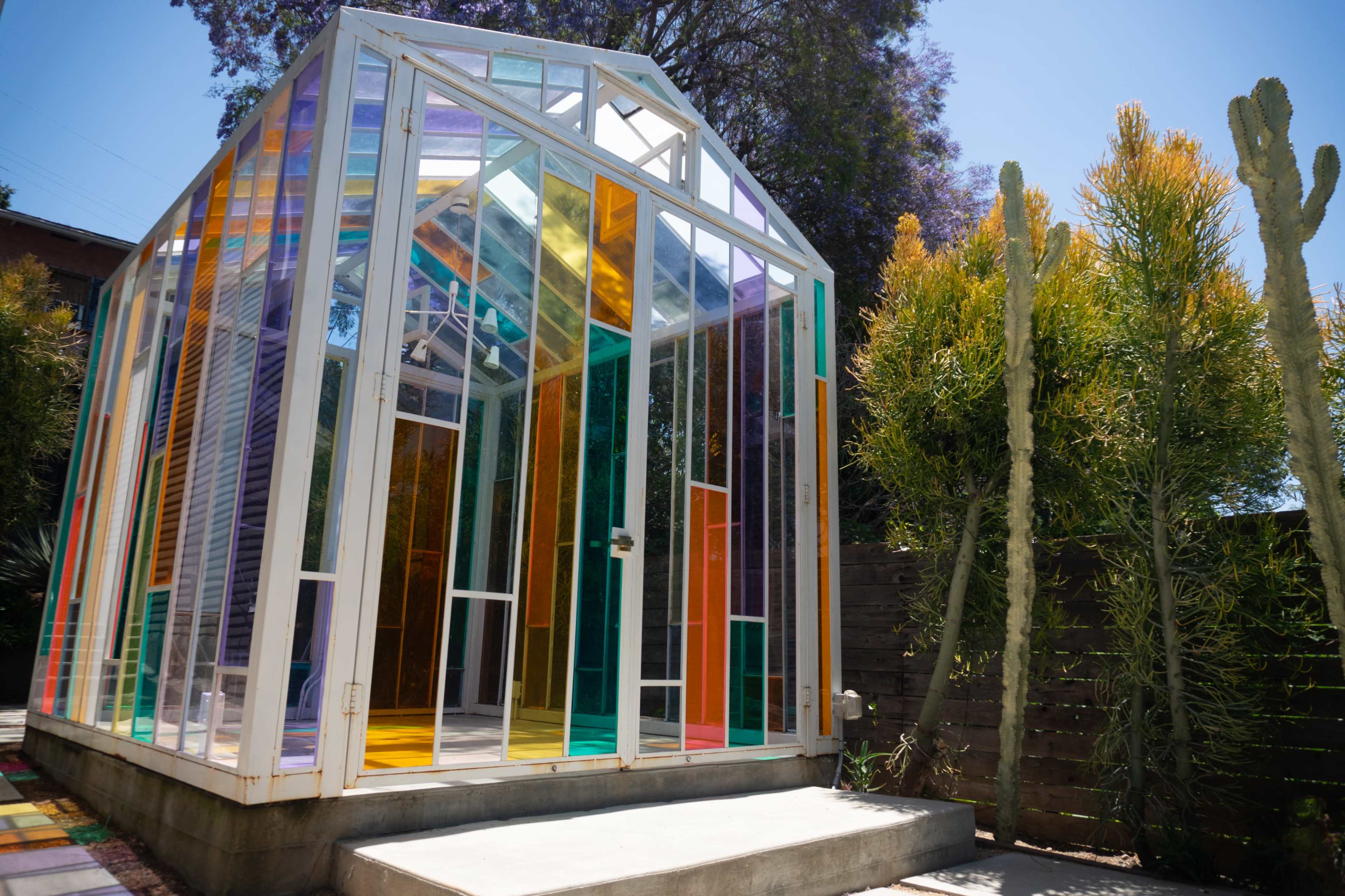 A colorful glass greenhouse surrounded by greenery and cacti.