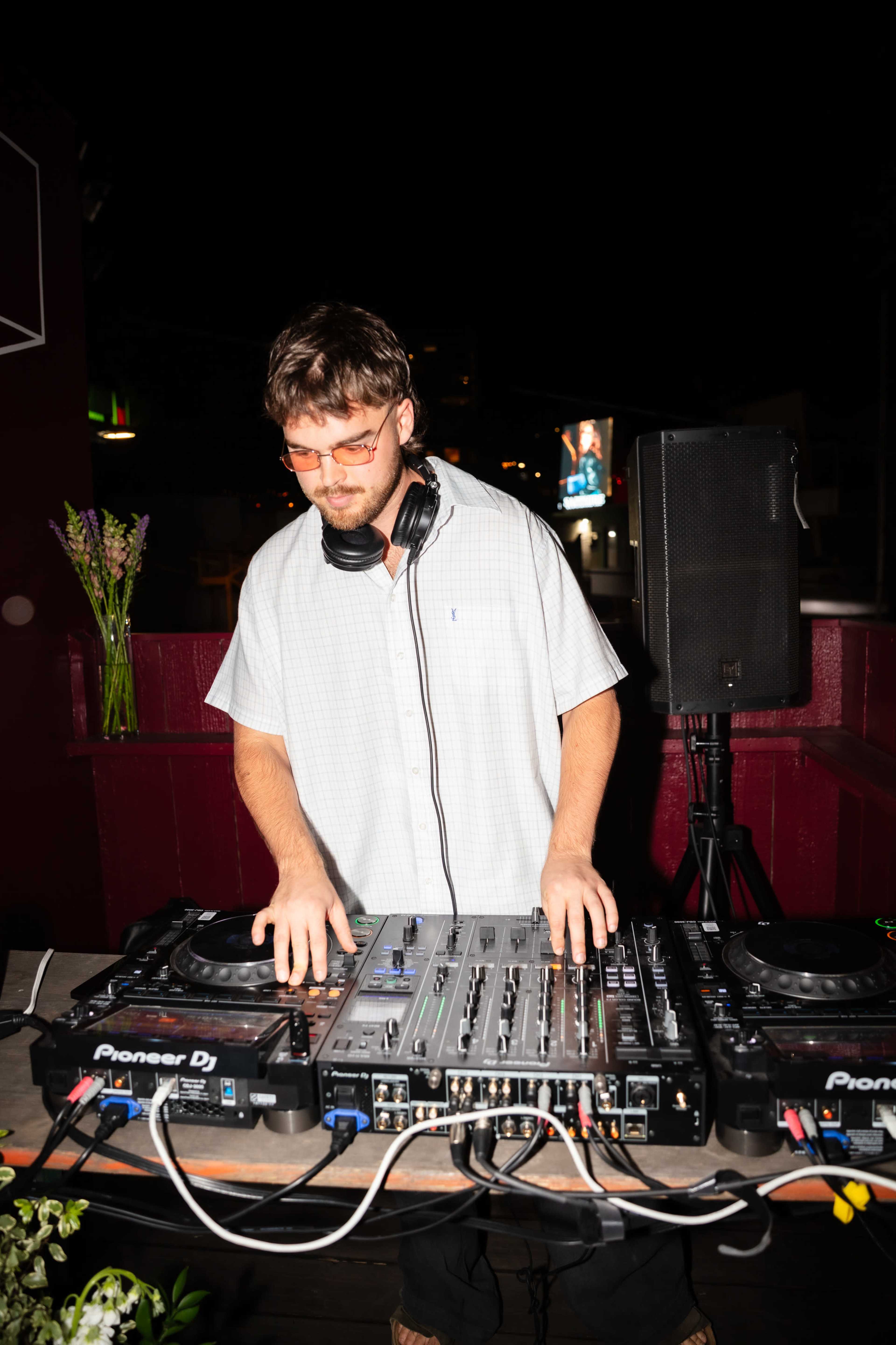 A DJ is surrounded by equipment while performing at an outdoor venue at night.