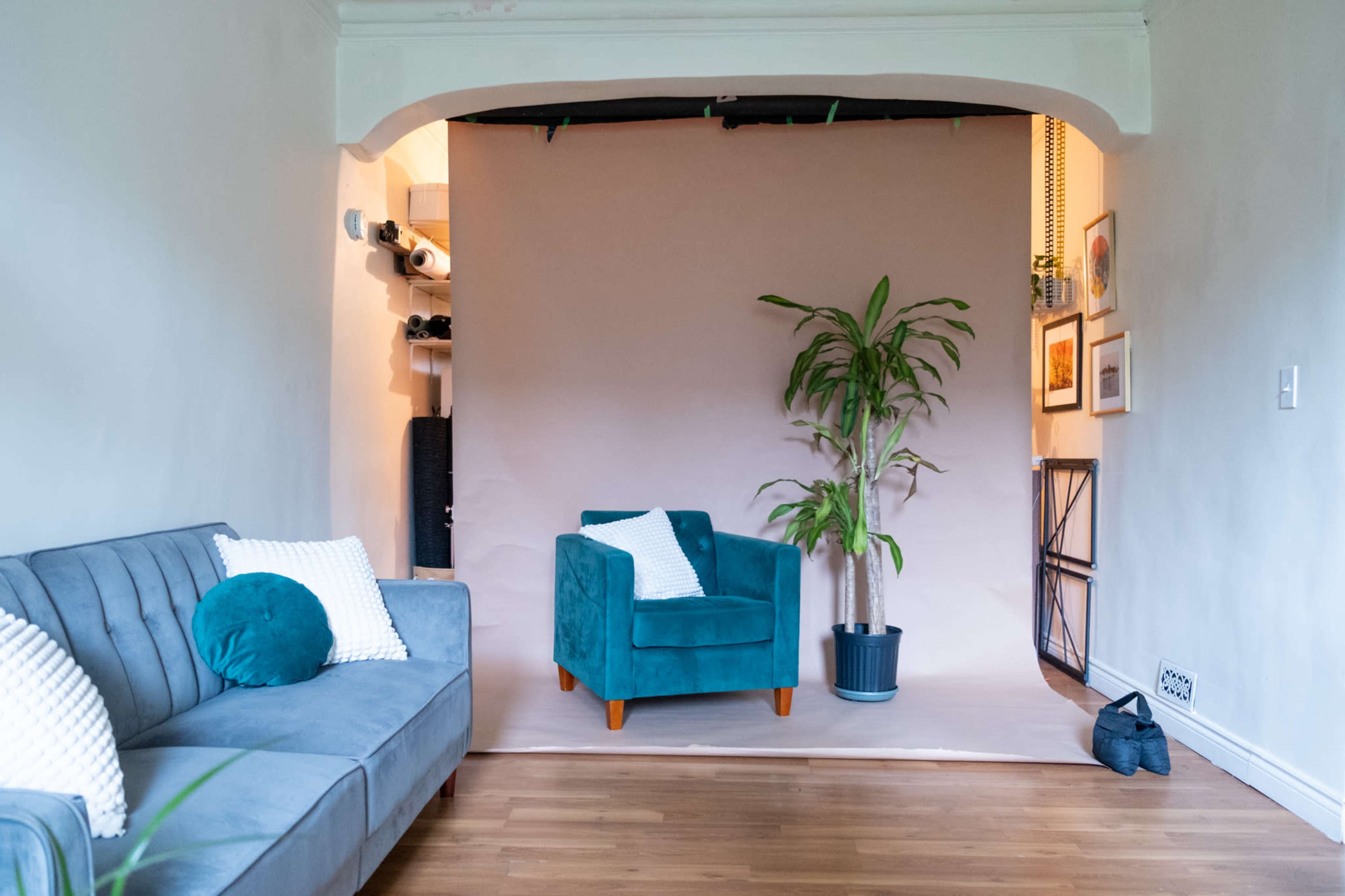 A turquoise armchair and a potted plant are positioned against a neutral backdrop in a room with hardwood flooring.