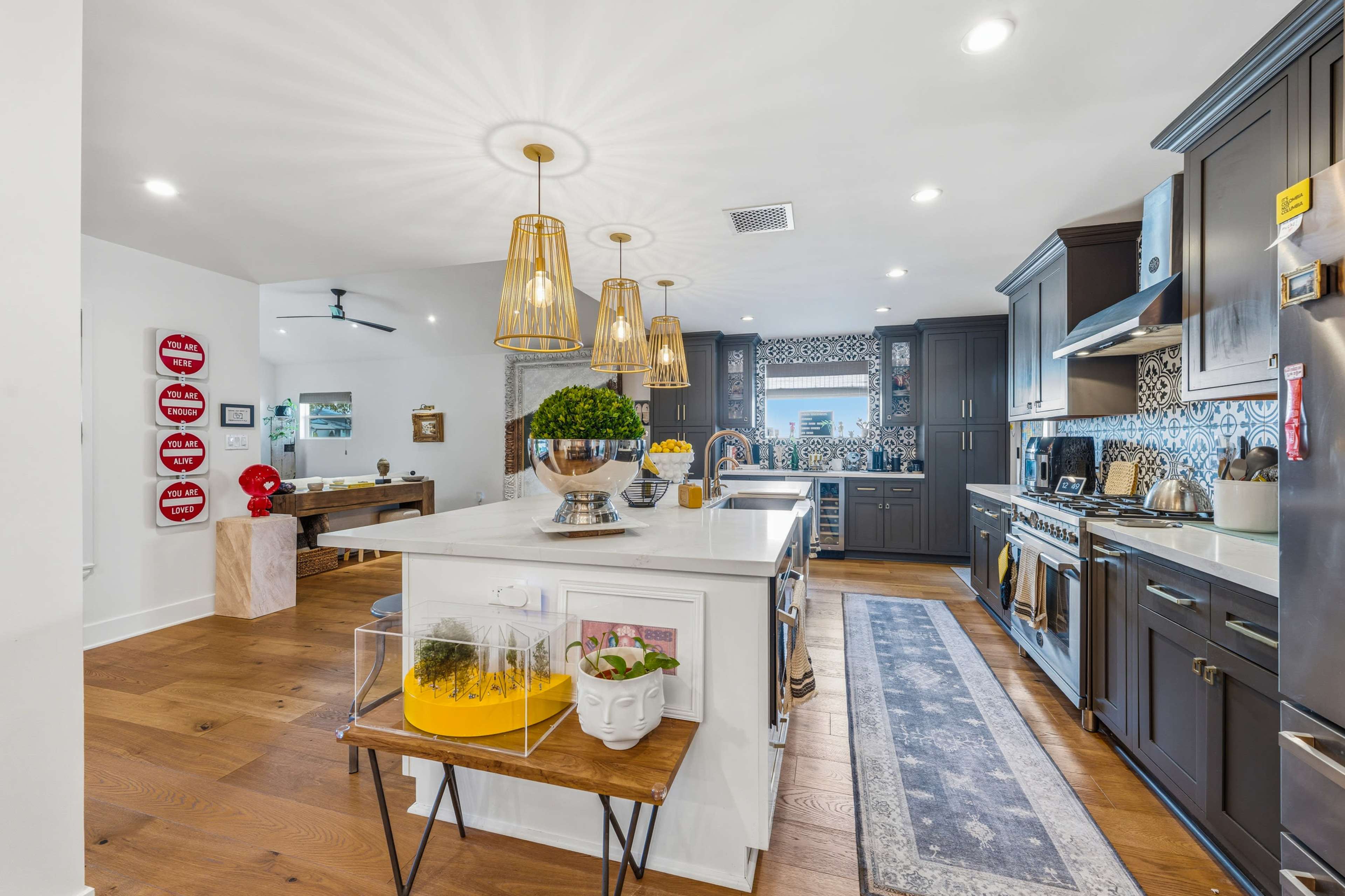 The image shows a modern kitchen with dark cabinetry, pendant lighting, and a central island featuring decorative items.