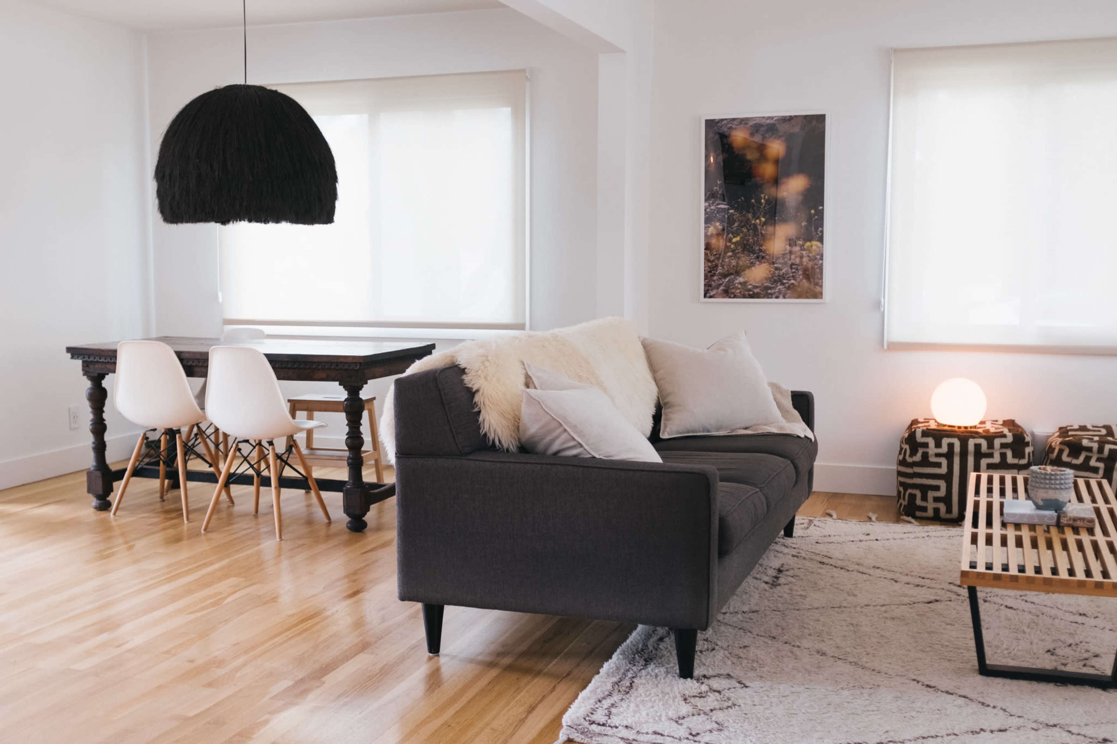 A modern living room with a gray sofa, a wooden dining table with white chairs, and a patterned rug on a wooden floor.