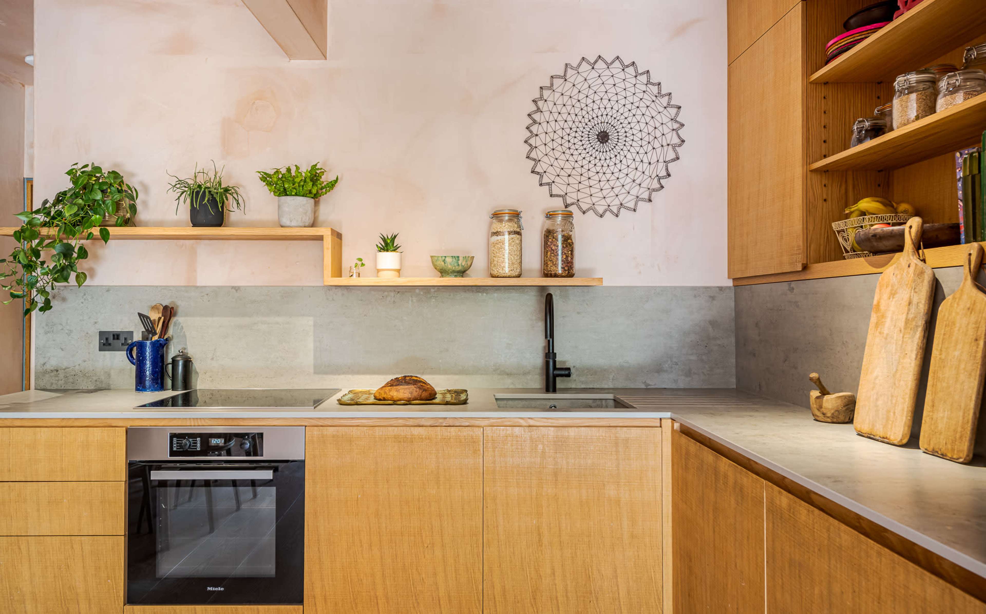 A modern kitchen features wooden cabinets, a concrete countertop, and various plants and decorative items on shelves.
