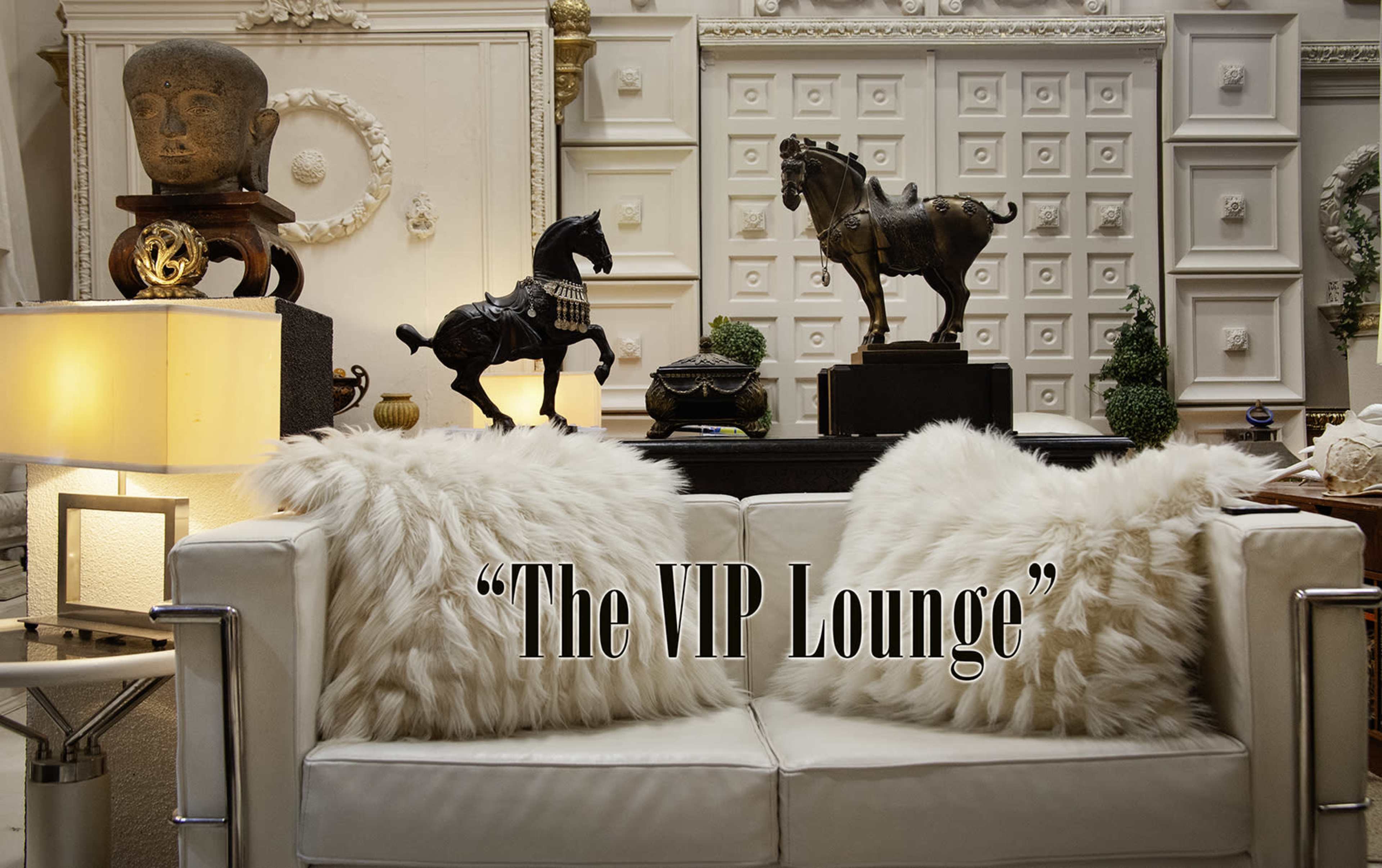 The image features a well-decorated lounge area with a white couch adorned with fluffy pillows, flanked by decorative sculptures, including a horse and a bust, set against an ornate backdrop.