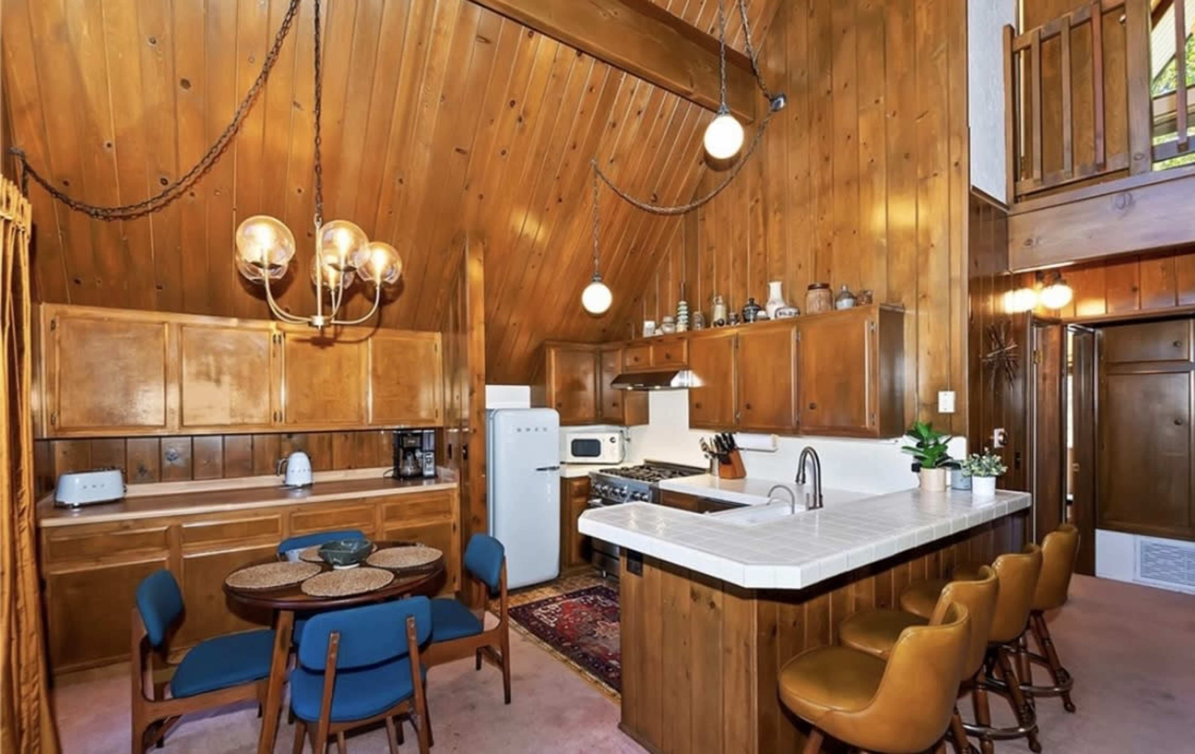A wooden-paneled kitchen and dining area featuring a round table with chairs, a white counter, and various kitchen appliances.