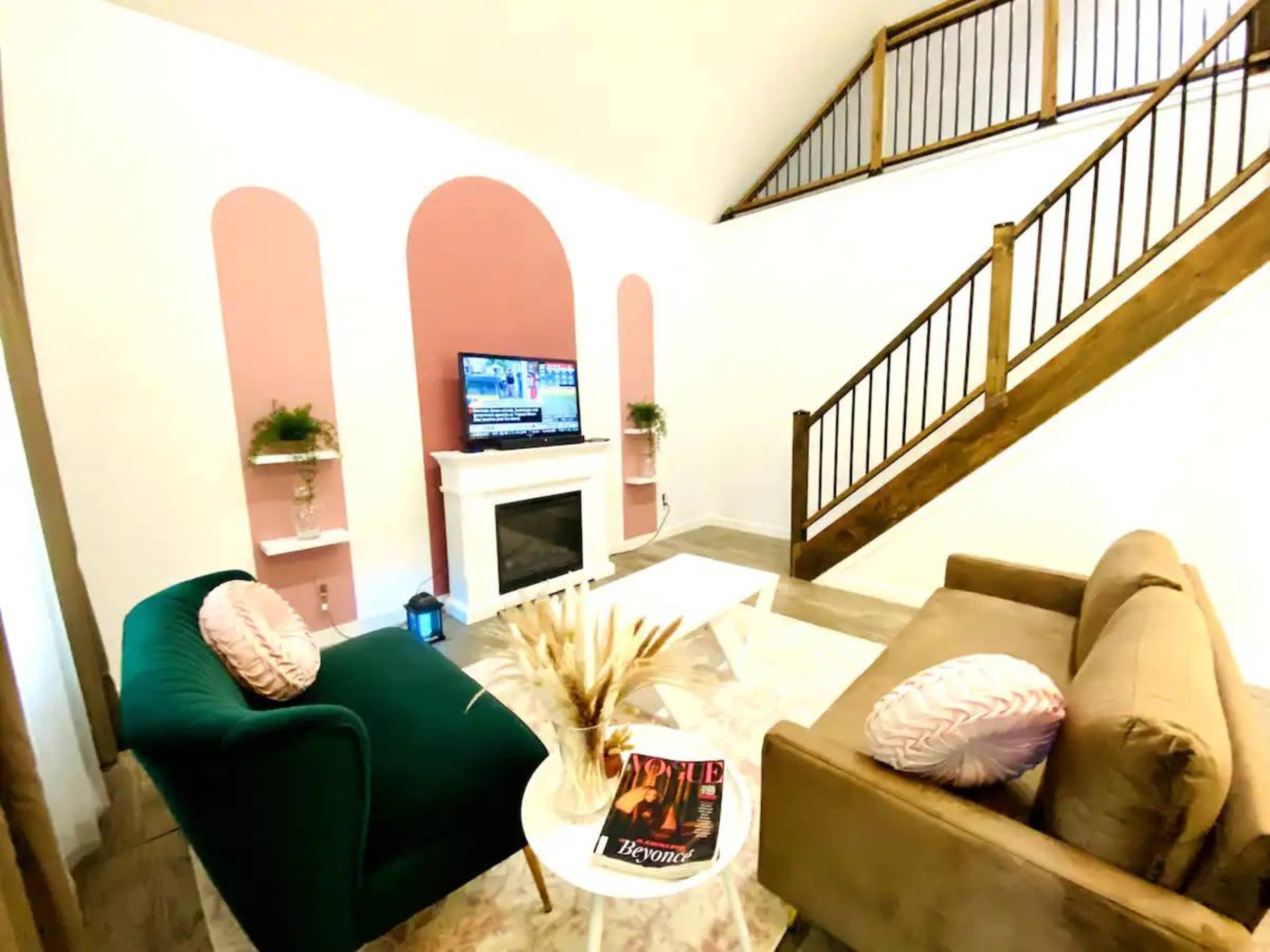 A modern living room featuring a television above a white fireplace, two sofas in contrasting colors, and a staircase in the background.