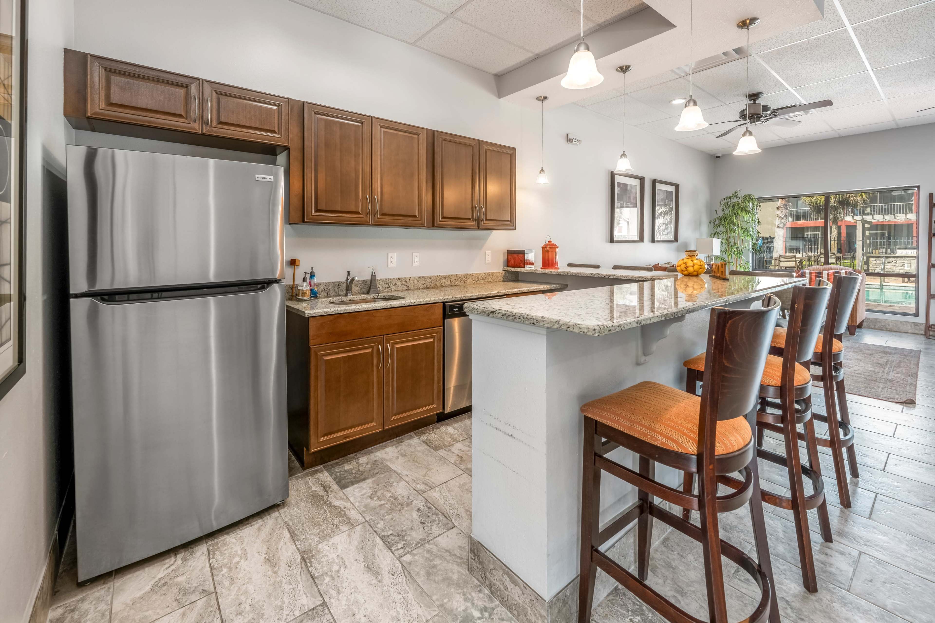 A modern kitchen features wooden cabinets, stainless steel appliances, and a bar with high stools.
