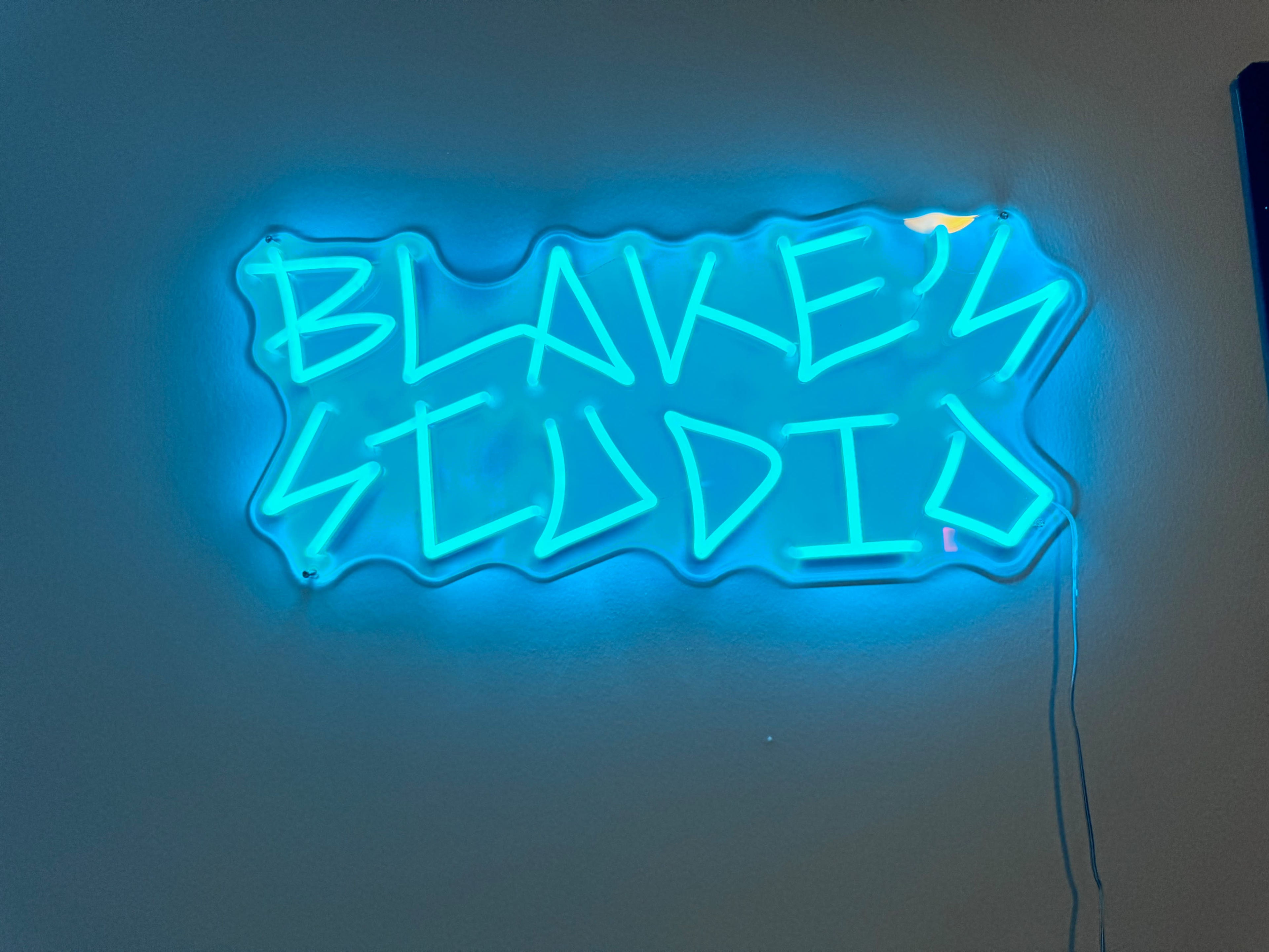A blue neon sign displaying the text "BLAKE'S STUDIO" is mounted on a wall.