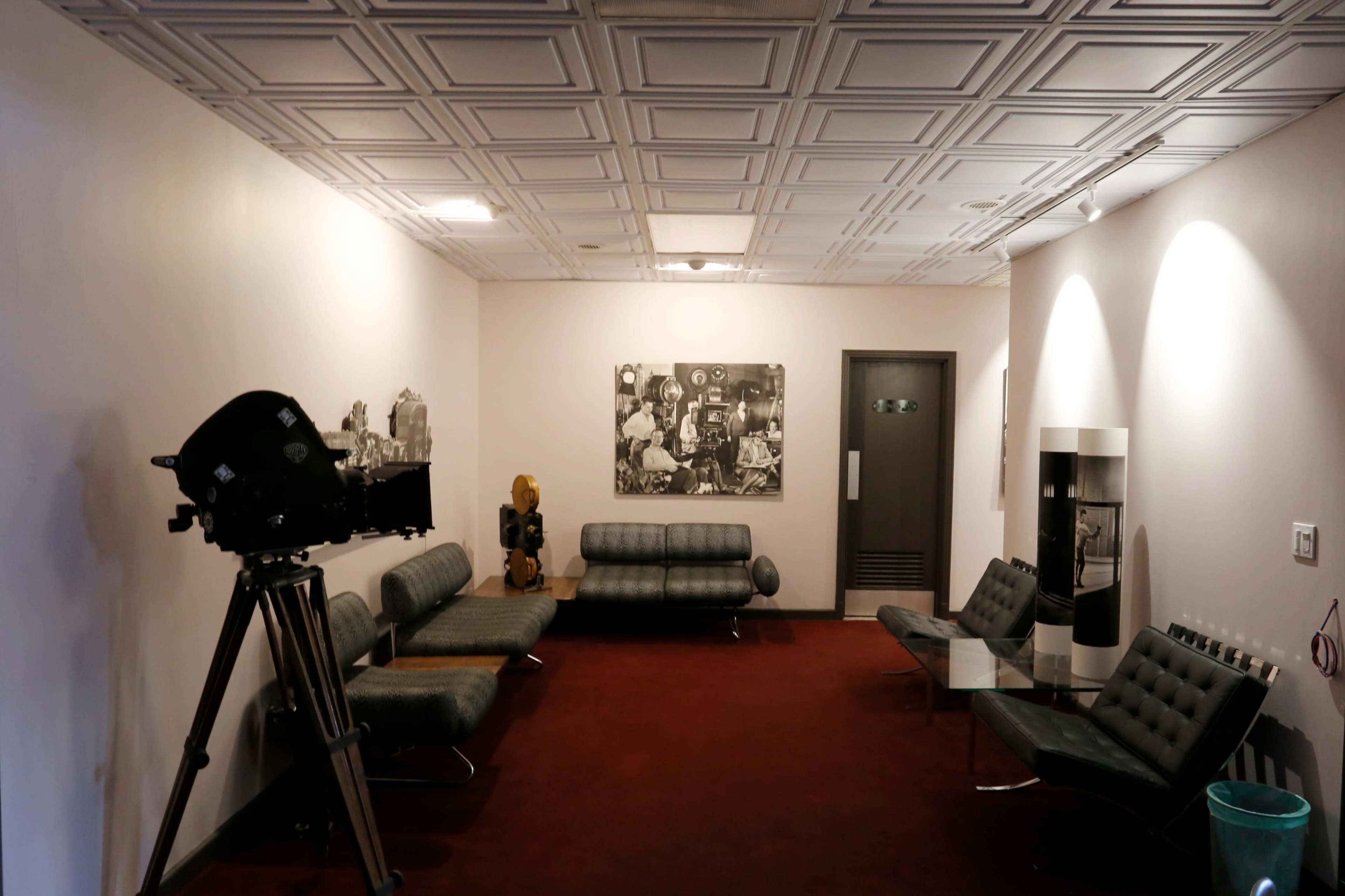 A waiting room features grey sofas, a large film camera on a tripod, and a black-and-white photograph on the wall.