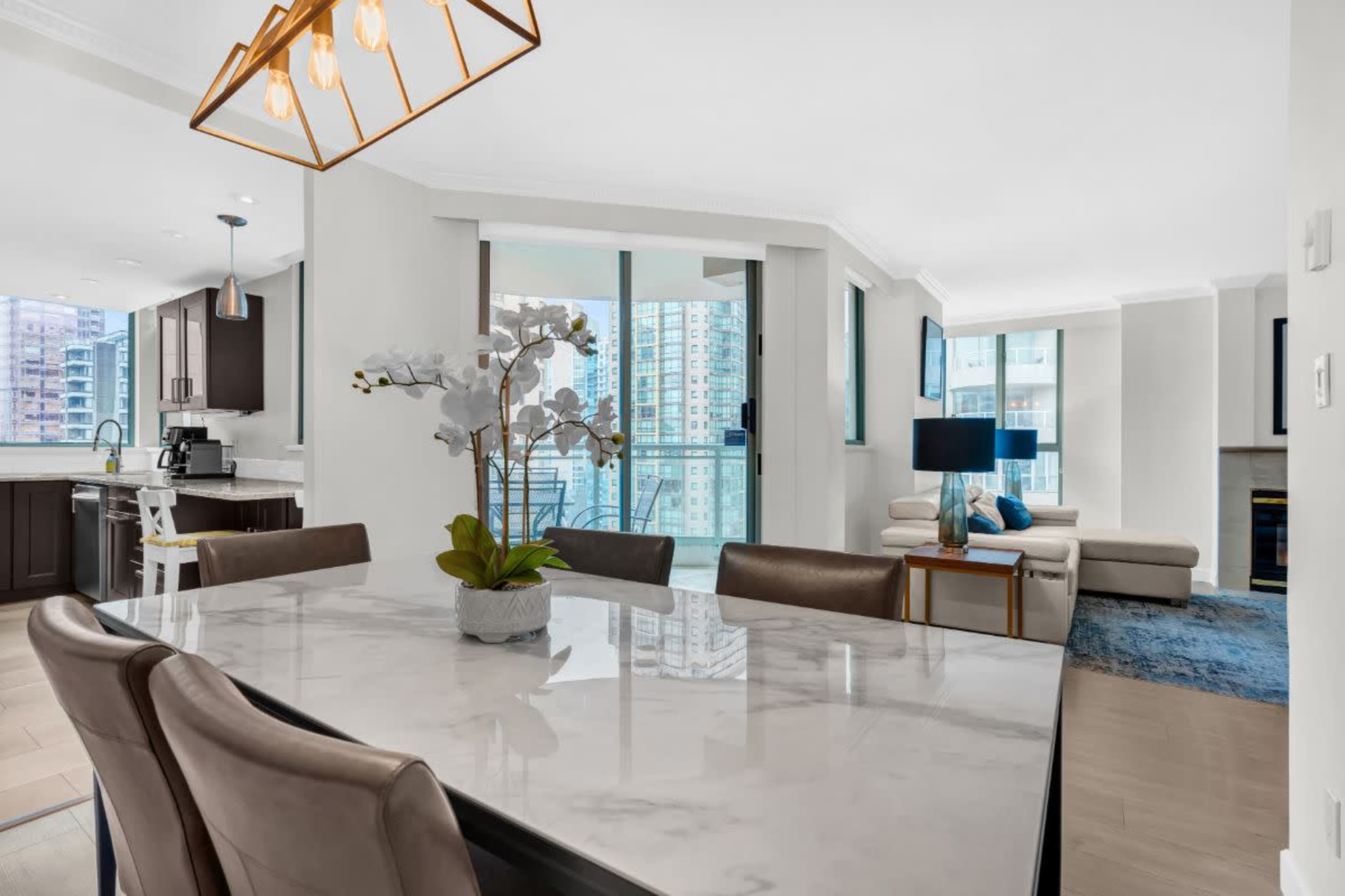 A modern dining area features a marble table with leather chairs, surrounded by a bright and airy living space with large windows and contemporary furnishings.