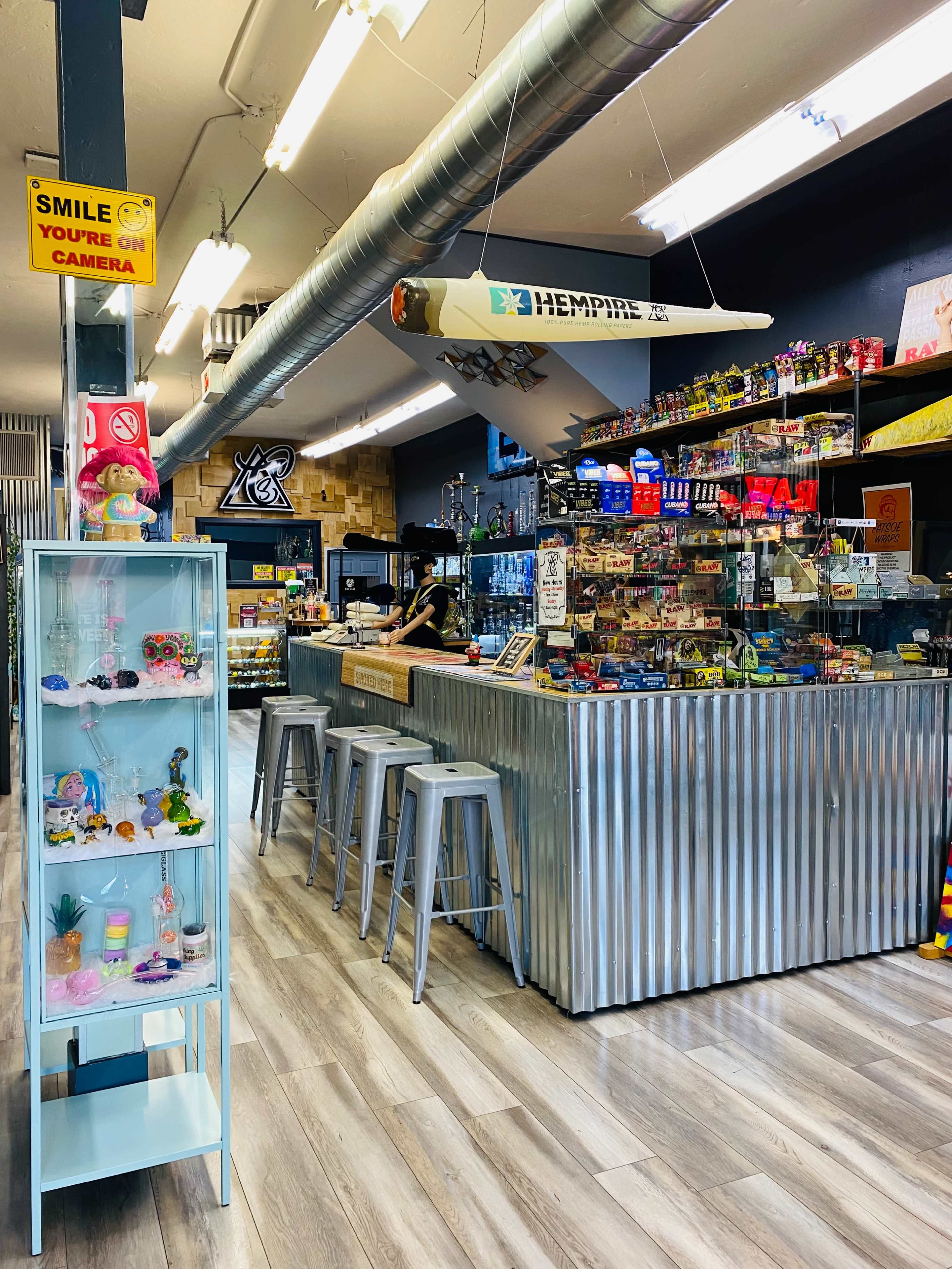 The interior of a shop featuring a metal counter, shelves filled with various merchandise, and a display case with colorful items near the entrance.