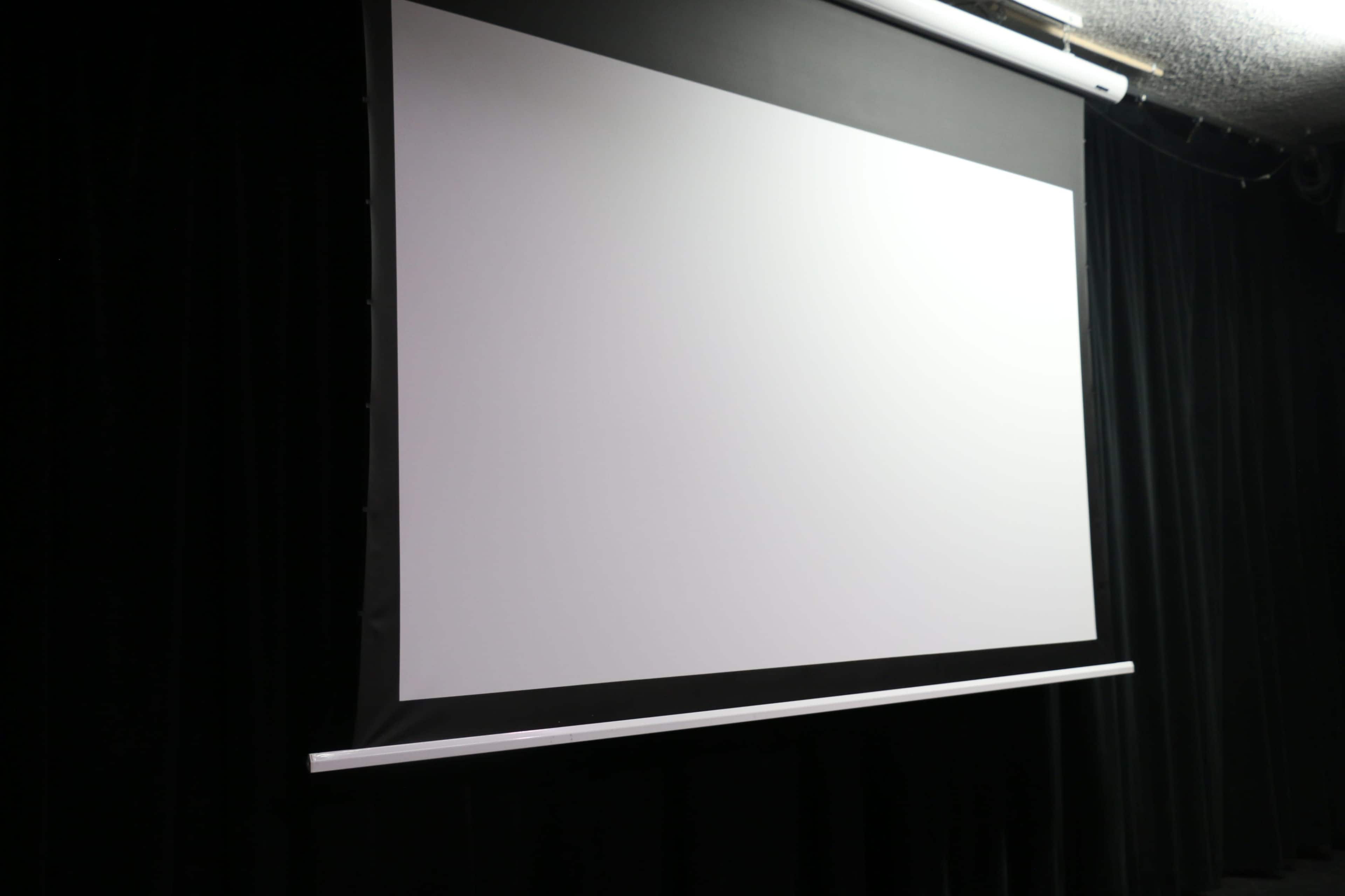 A blank projection screen is mounted against a black curtain backdrop.