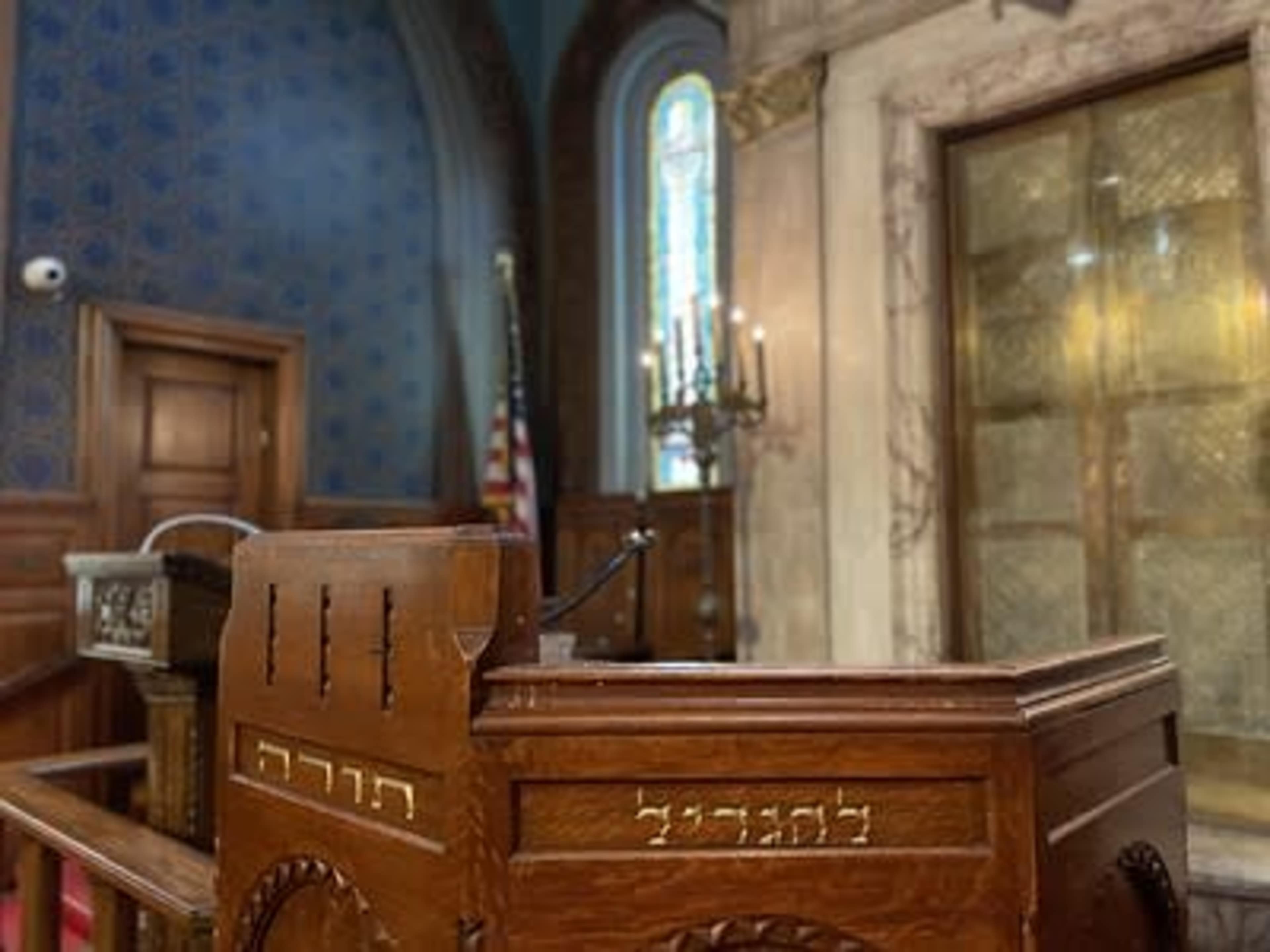 A wooden podium in a synagogue, with a decorative background and a stained glass window.