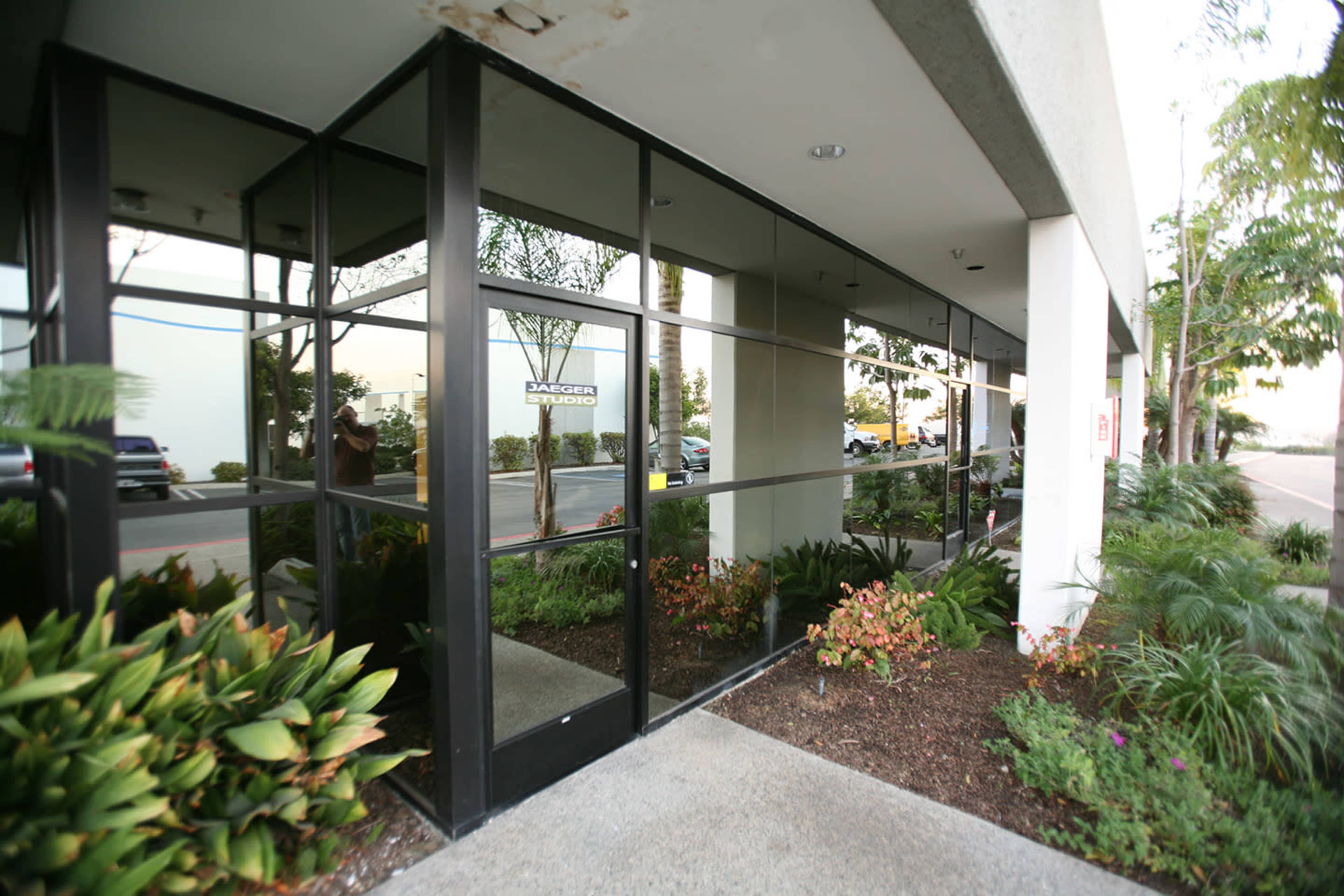 A modern building entrance with large glass windows and landscaped greenery in front.