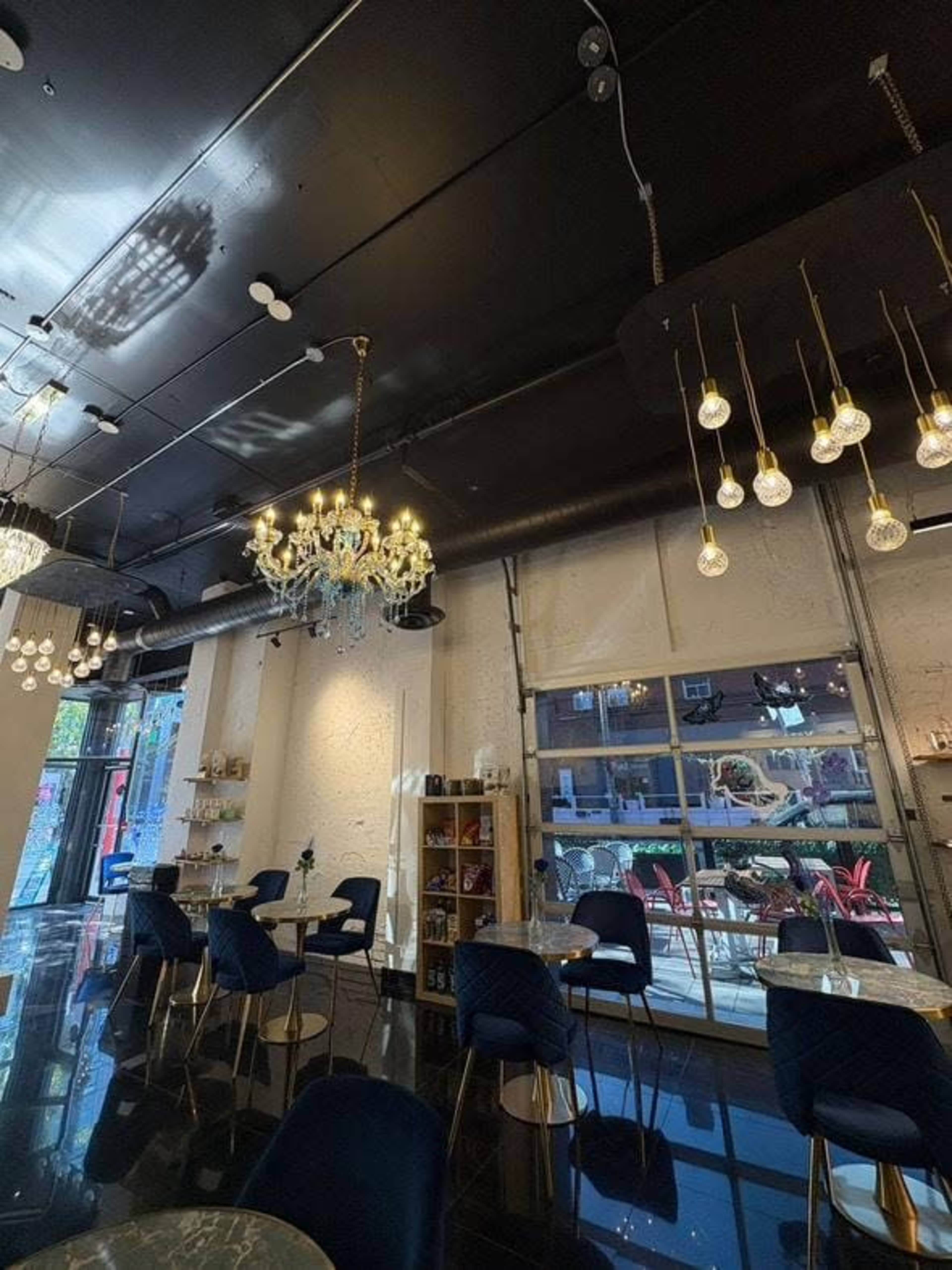 The image shows a modern cafe interior with elegant lighting fixtures, including a chandelier and hanging bulb lights, set against a backdrop of dark walls and shiny floors.