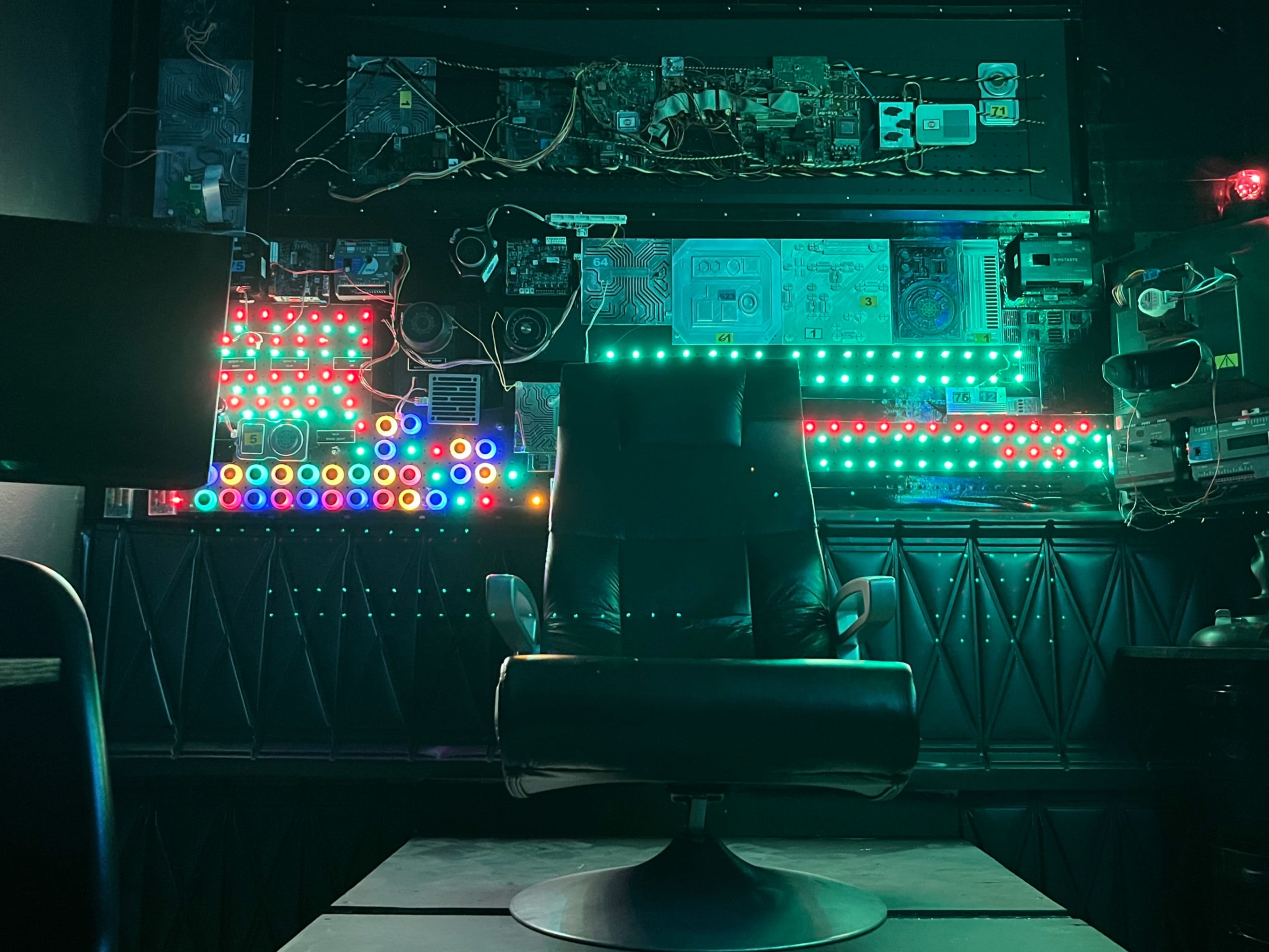 A black swivel chair is positioned in front of a wall featuring colorful LED lights and various electronic components.