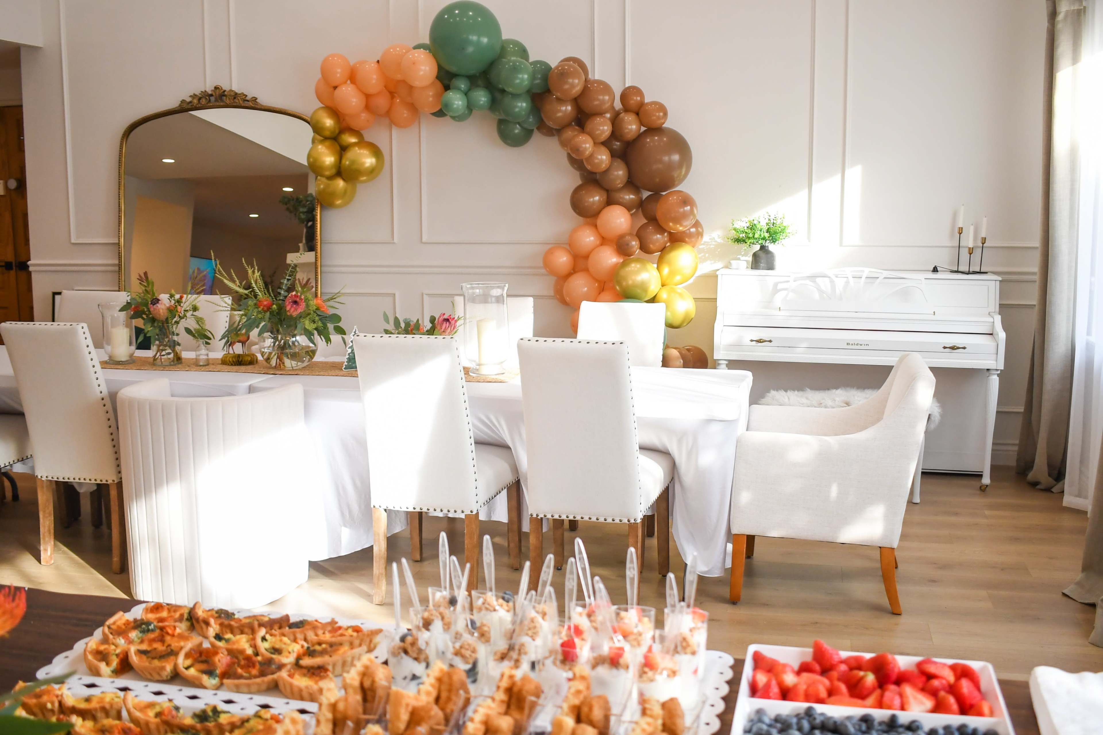 The scene features a neatly arranged dining area with a table set for a celebration, decorated with balloons and a spread of various appetizers.