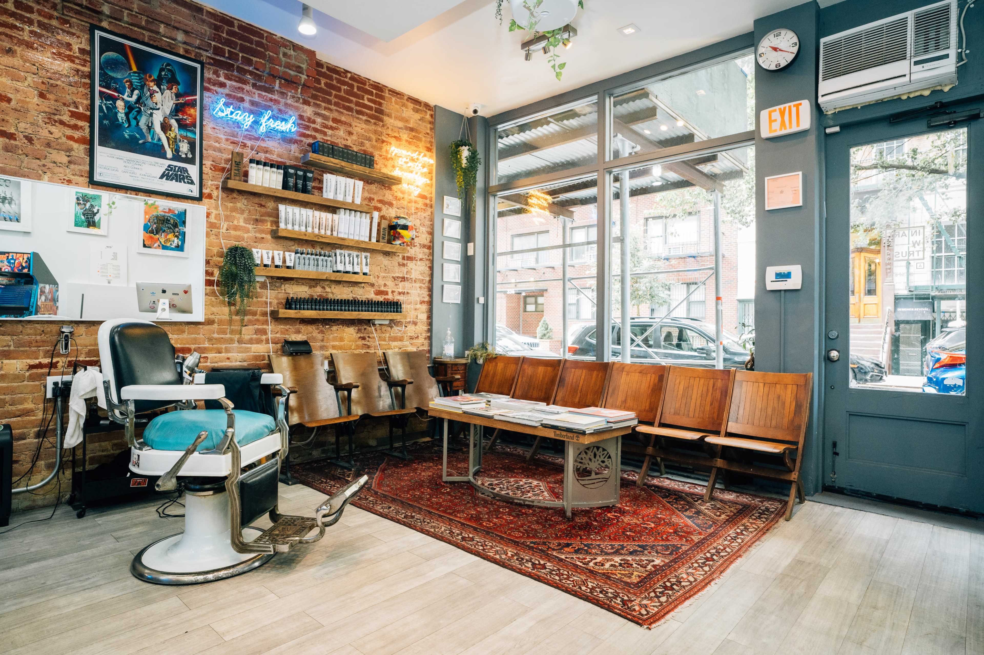 A barbershop interior with brick walls, vintage seating, a barber chair, and large windows letting in natural light.