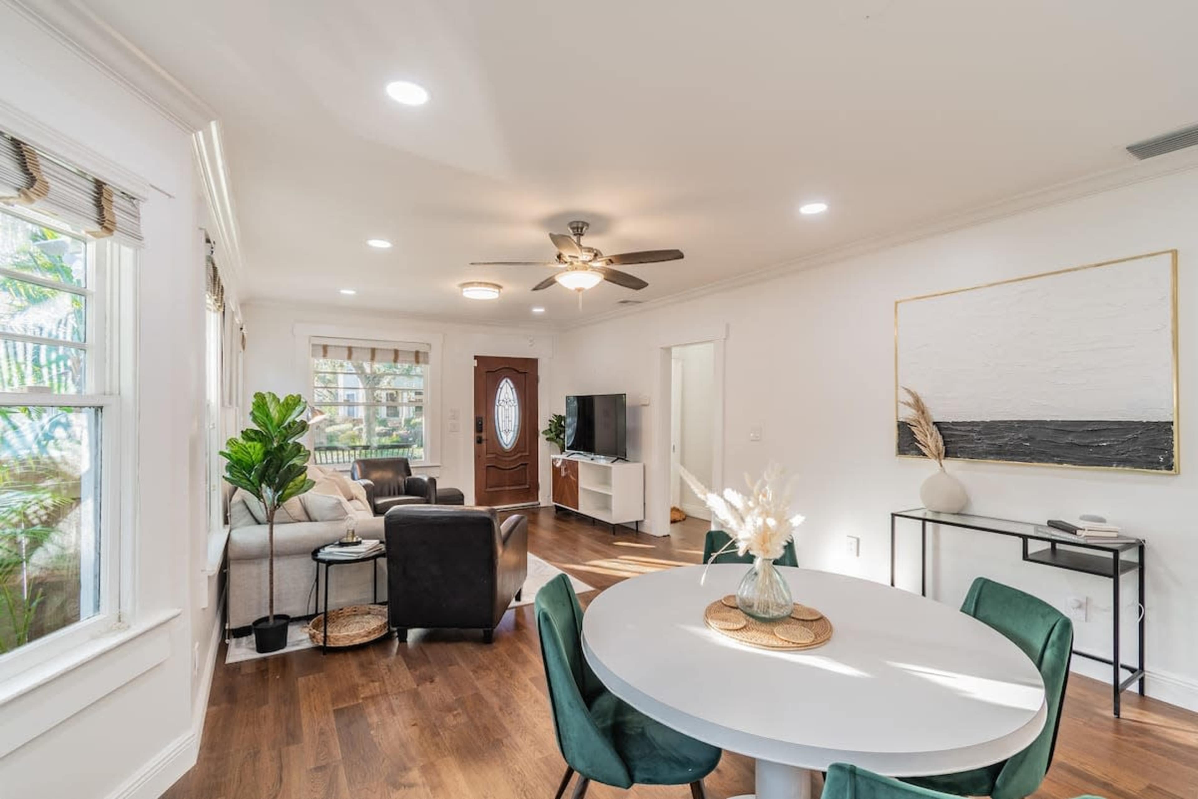 A modern living space with a circular dining table, a gray sofa, a television, and large windows allowing natural light to enter.