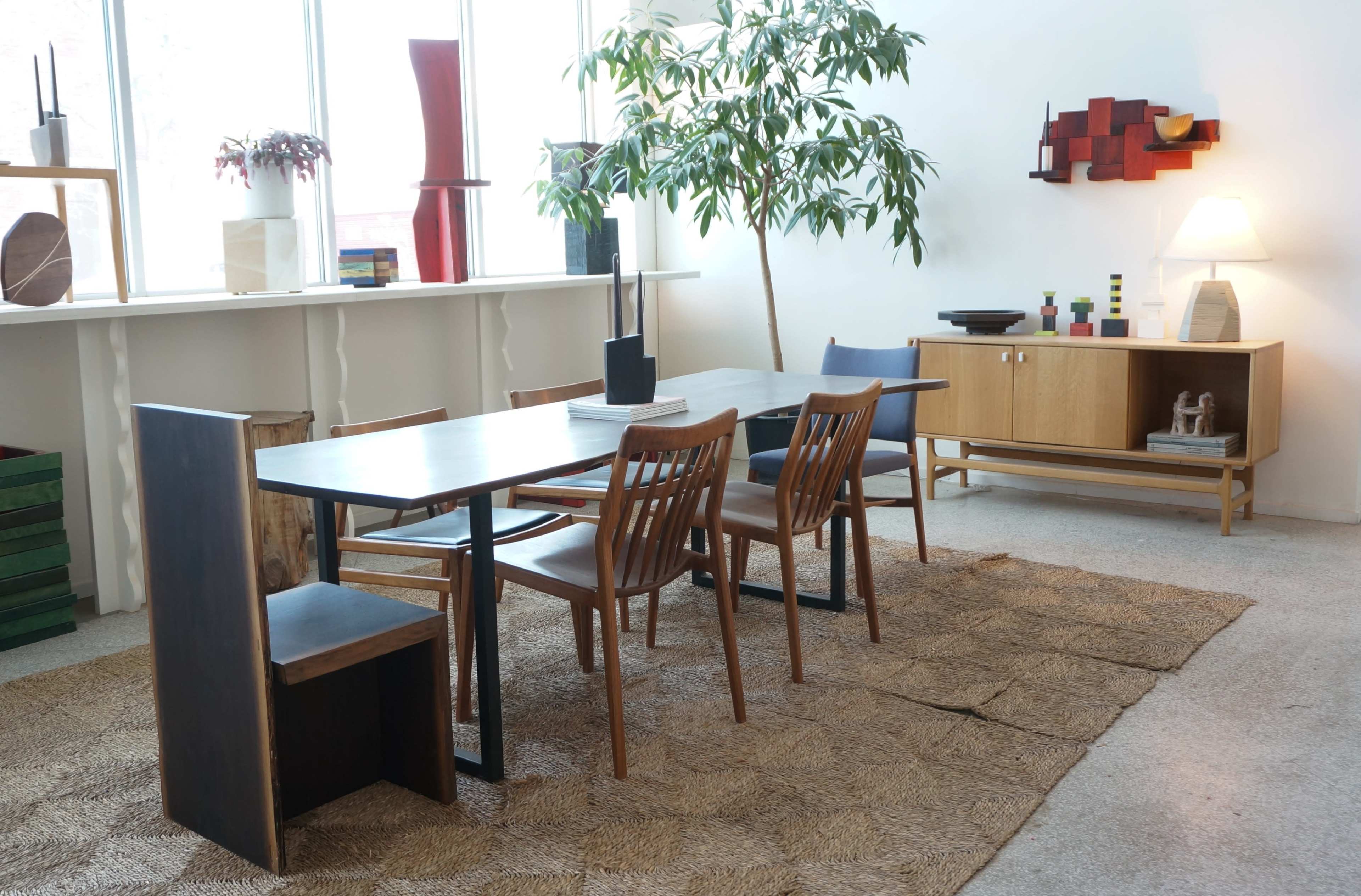 The image features a modern dining area with a wooden table surrounded by chairs, a large potted plant, and decorative elements on the walls and shelves.