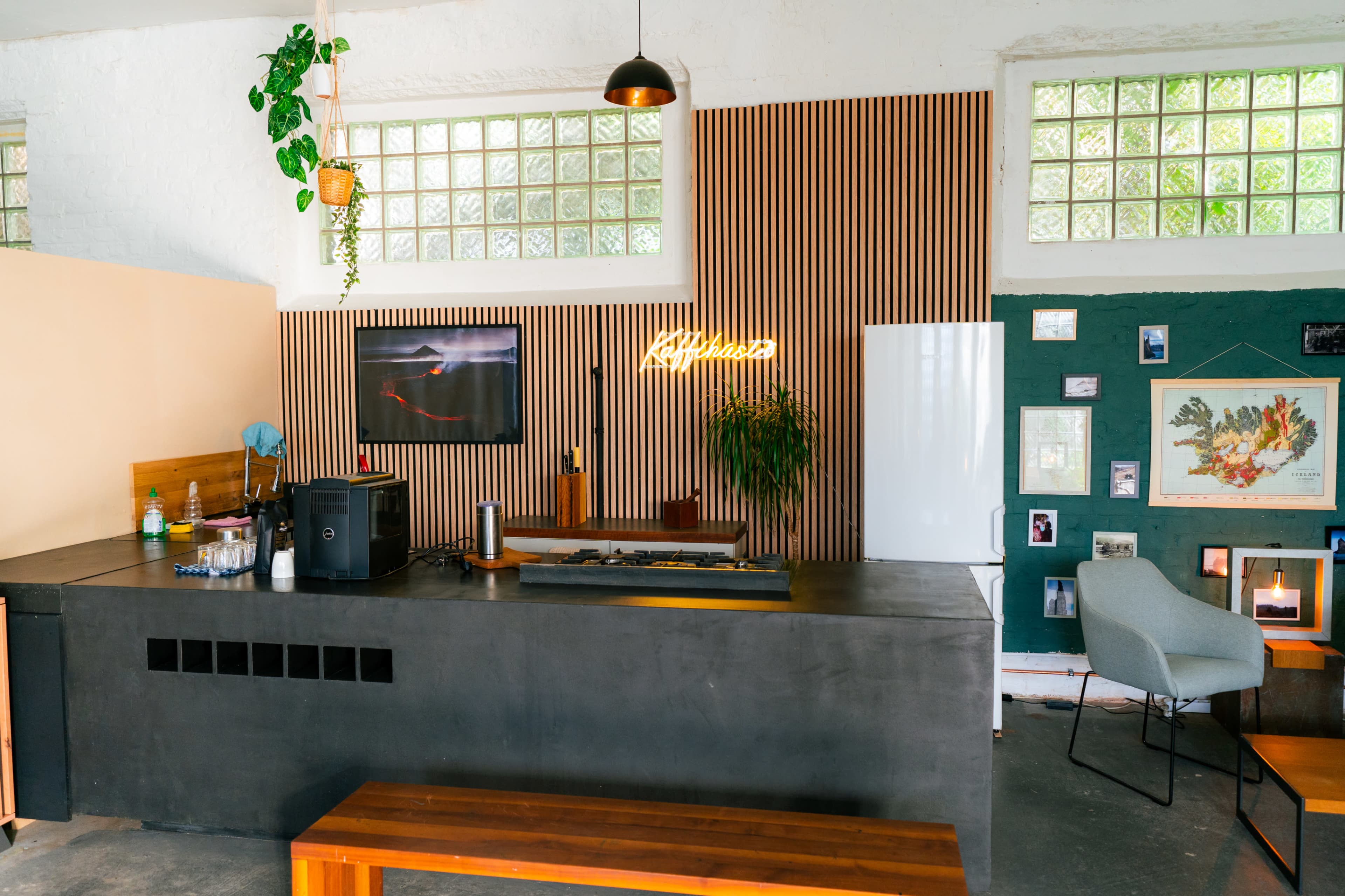 The image shows a modern café interior featuring a sleek black counter, wooden accents, and various plants, with framed pictures and art on the walls.