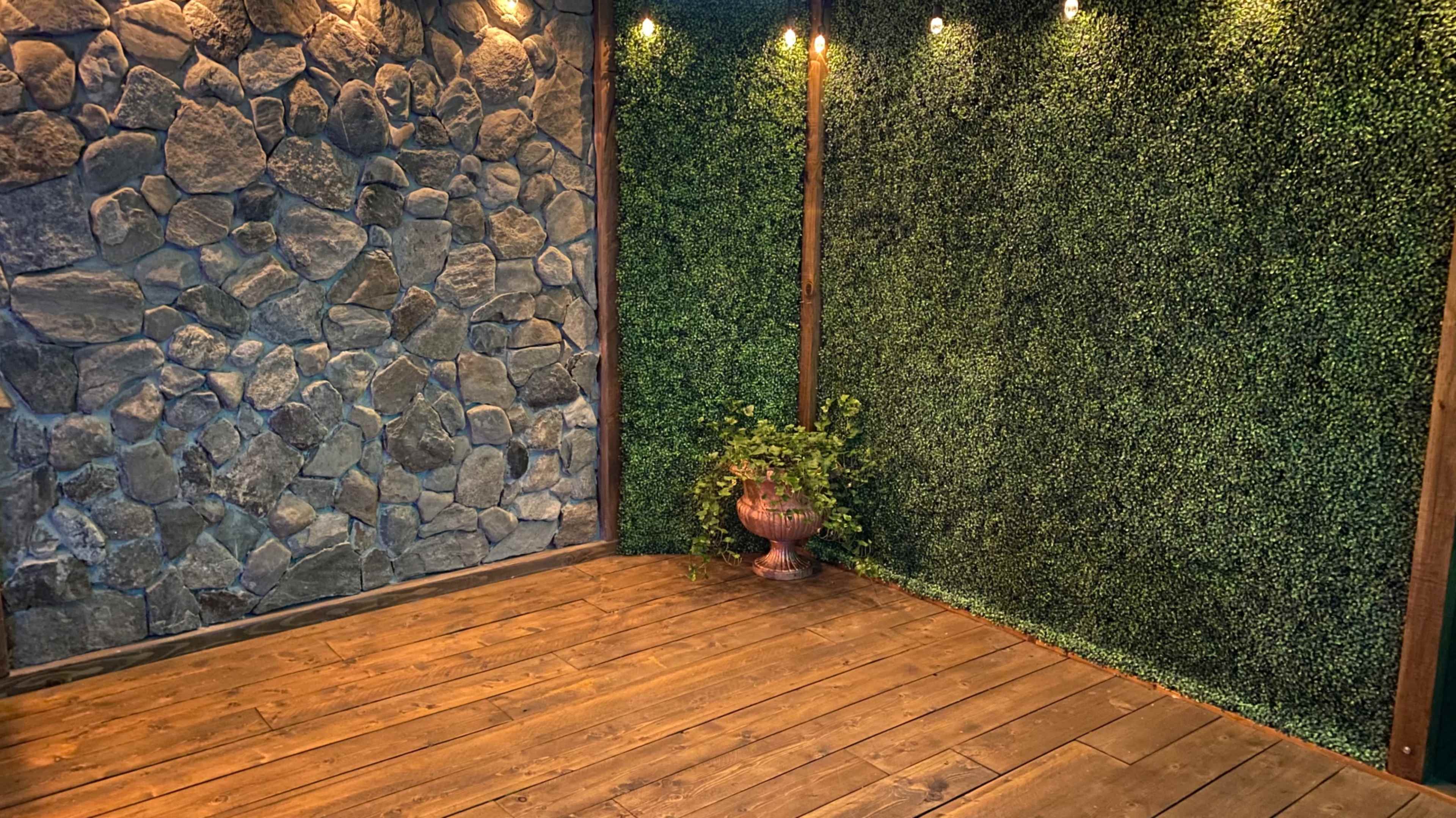 A corner of a room with one wall made of stone and another covered in green foliage, complemented by wooden flooring and soft lighting.