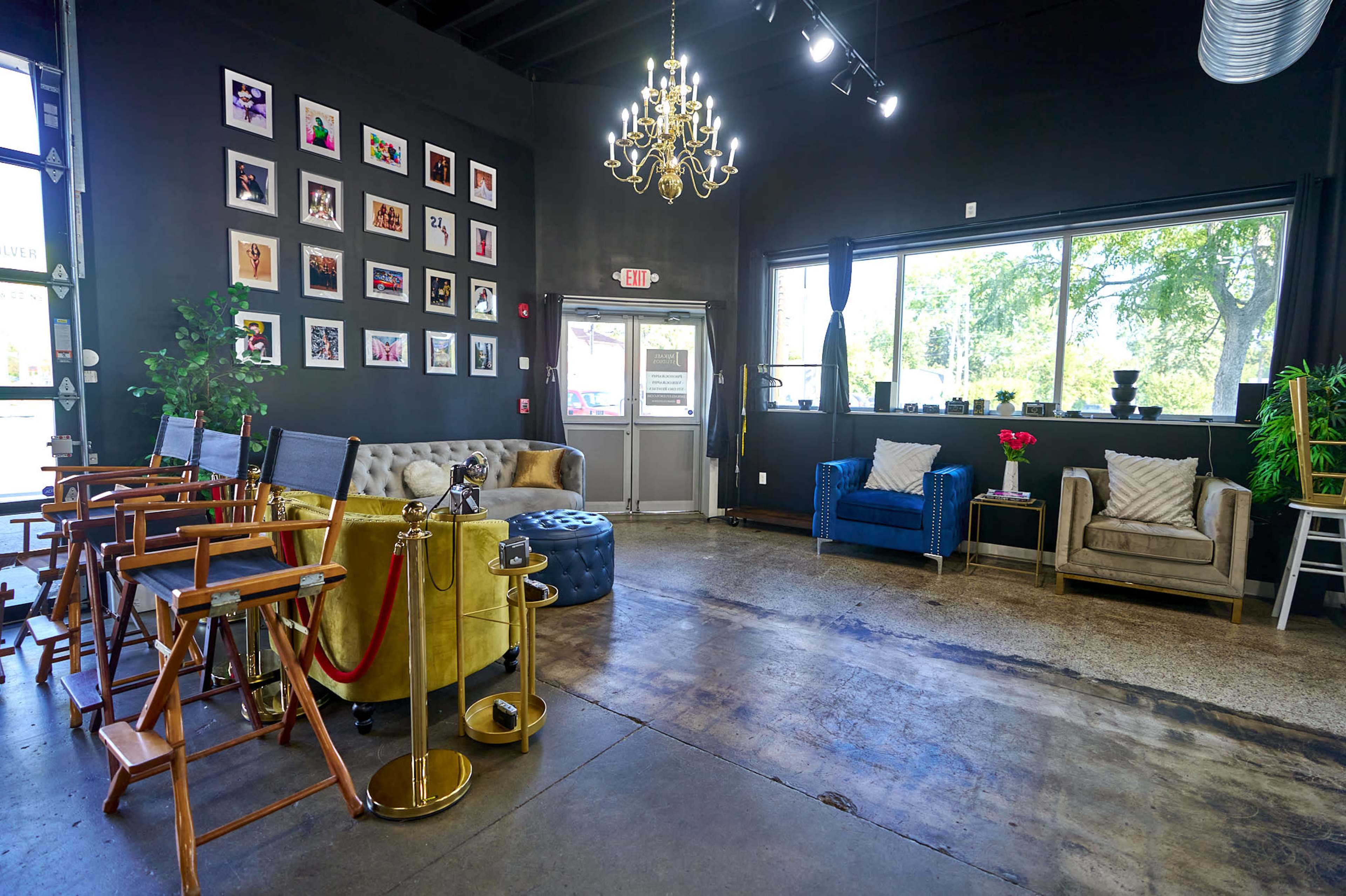 A modern interior space with a seating area featuring colorful chairs, a chandelier, and a wall adorned with framed photographs.