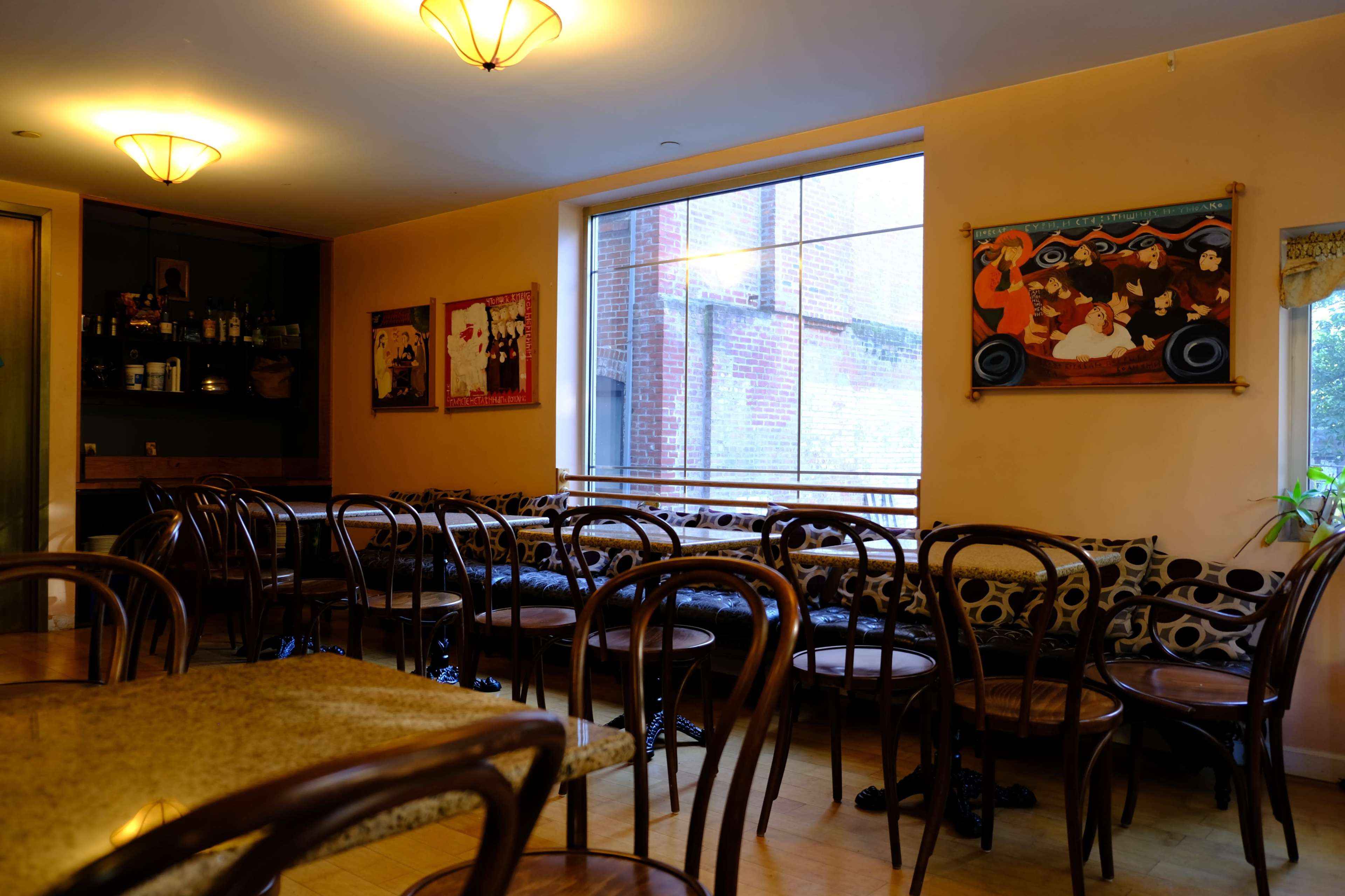 A cozy café interior with wooden chairs arranged around tables and large windows allowing natural light to enter.