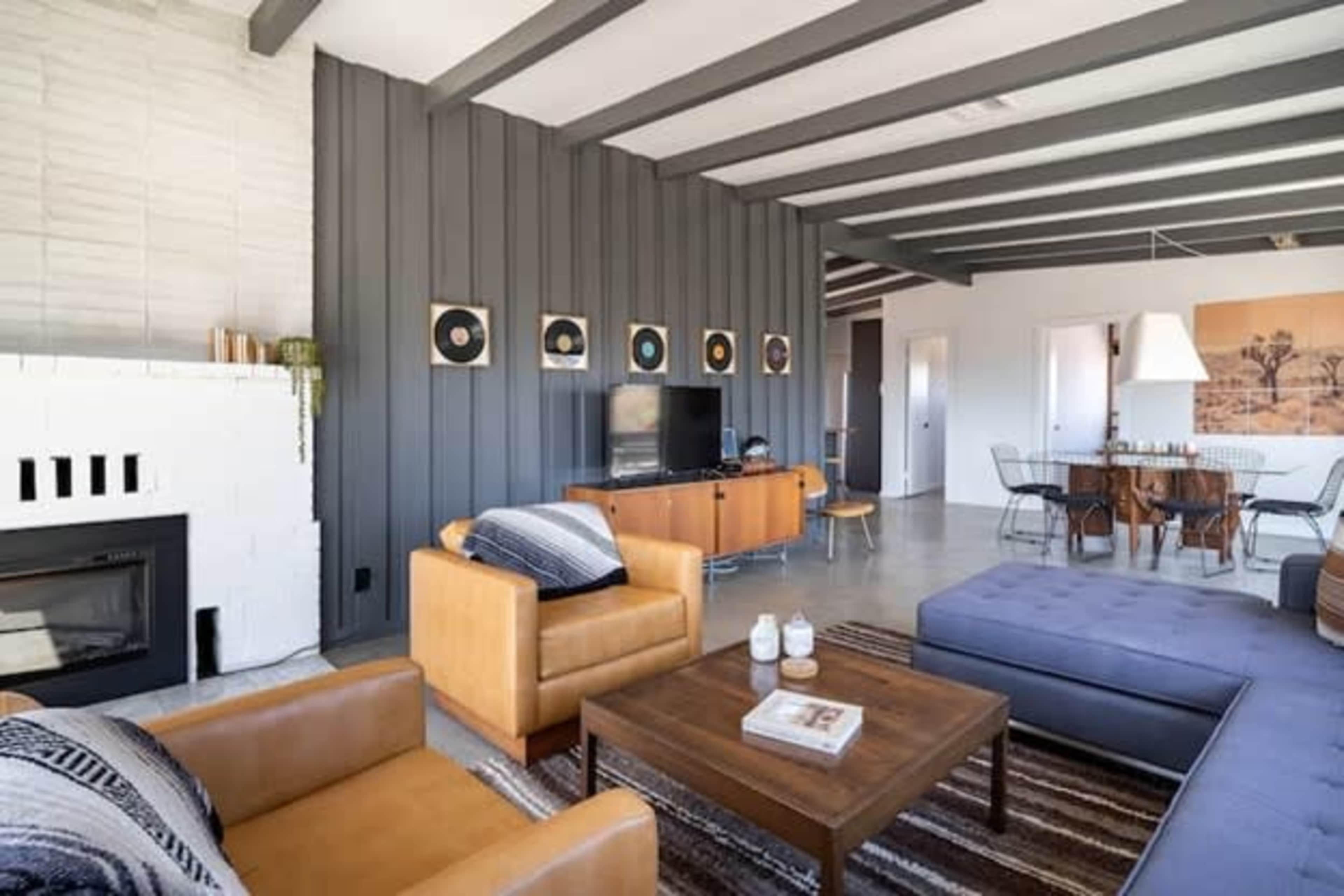 A modern living room with a blend of leather furniture, a wooden coffee table, a television setup, and a dining area in the background.